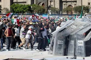 சனிக்கிழமையன்று (நவம்பர் 15) மெக்சிகோ நகரில் உள்ள தேசிய மாளிகையின் வெளியில் கூடிய ஆர்பாட்டக்காரர்கள், அவர்களைக் கட்டுப்படுத்தும் காவல்துறையினர்.