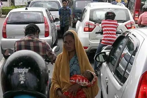 வாகனங்கள் நிறைந்த சாலையில் குழந்தையைக் காட்டி பிச்சை எடுக்கும் பெண்.