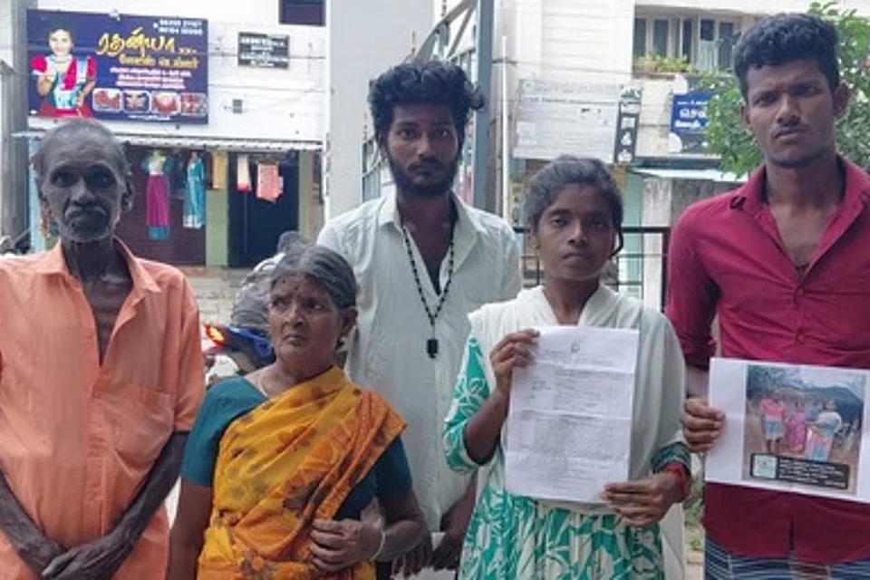 குறிப்பாணையைக் கையில் ஏந்திக்கொண்டு நிற்கும் கூலித் தொழிலாளி சுகன்யா மற்றும் அவரின் குடும்பத்தினர்.