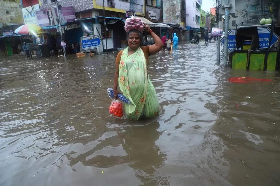 வெள்ளம் போல் தேங்கி நிற்கும் மழை நீரில் காய்கறிகள் வாங்கிச் செல்லும் பெண். 