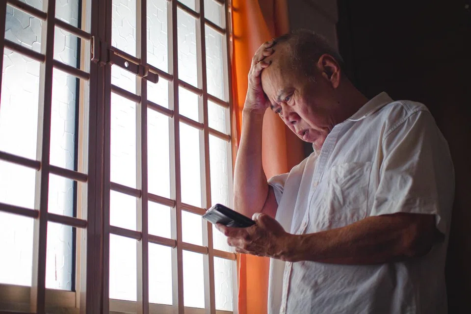 Low angle shot of Senior Asian man having a hard time, pressing his head while holding phone