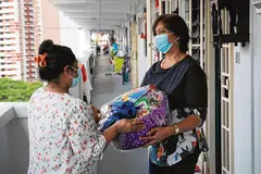 சிரமமான சூழலை எதிர்நோக்கும் ஒற்றைப் பெற்றோரான திருவாட்டி சிவா (இடது), உதவிப் பொருட்களைப் பெற்றுக்கொள்கிறார். படம்: ஸ்ட்ரெய்ட்ஸ் டைம்ஸ்