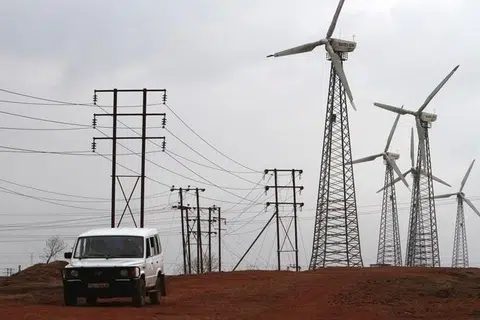 காற்றாலைப் பண்ணையில் உள்ள காற்றாலைகள், மின் கோபுரங்கள் நிறைந்த வழித்தடங்களைக் கடந்து  செல்கிறது ஒரு வாகனம். 