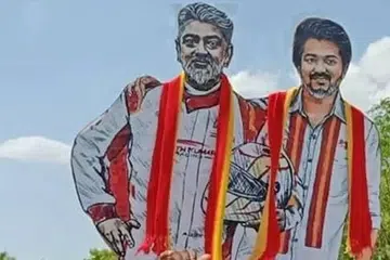 அஜித் கார்ப் பந்தய உடையிலும் விஜய் அரசியல் உடையிலும் காணப்படும் ‘கட்-அவுட்’ படத்தை மதுரையில் ஏந்தியிருக்கும் தவெக தொண்டர்கள்.