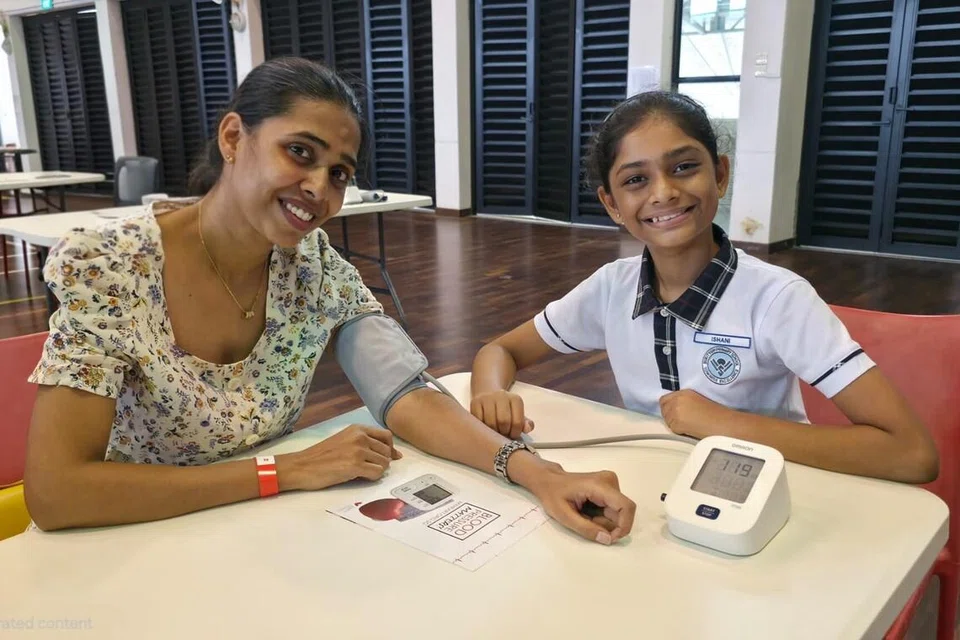 தாயார் வெண்ணிலா முனுசாமியின் ரத்த அழுத்தத்தை அளவிட  கண்காணிப்புக் கருவியை இ‌‌‌ஷானி சண்முகம் பயன்படுத்துகிறார்.