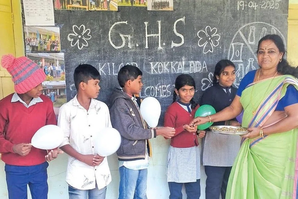 பள்ளிக்கு வரும் மாணவர்களுக்கு இனிப்புகளை வழங்கி வரவேற்கும் அரசுப் பள்ளி ஆசிரியர்.