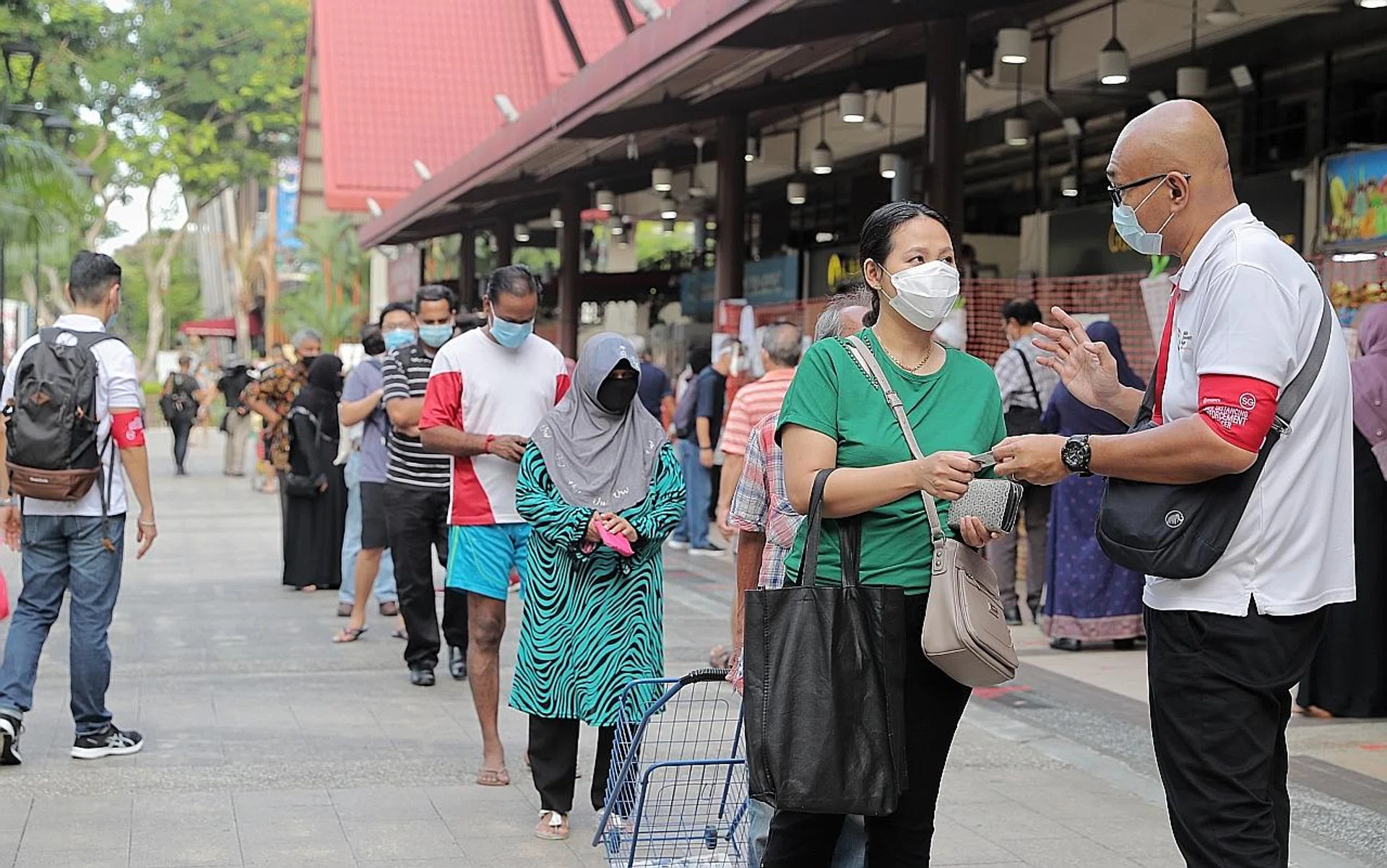 A safe distancing enforcement officer checking a shopper's IC number as she queues to enter Geylang Serai market. 