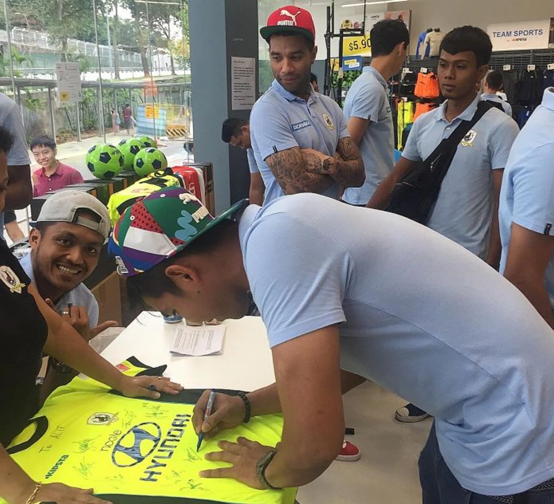 OFF-FIELD INITIATIVES:  Stags' goalkeeper Izwan Mahbud autographing a jersey at the club's launch of the Pentagon Football Academy at the Decathlon store in Bedok, as teammate Jermaine Pennant (wearing red cap) looks on.