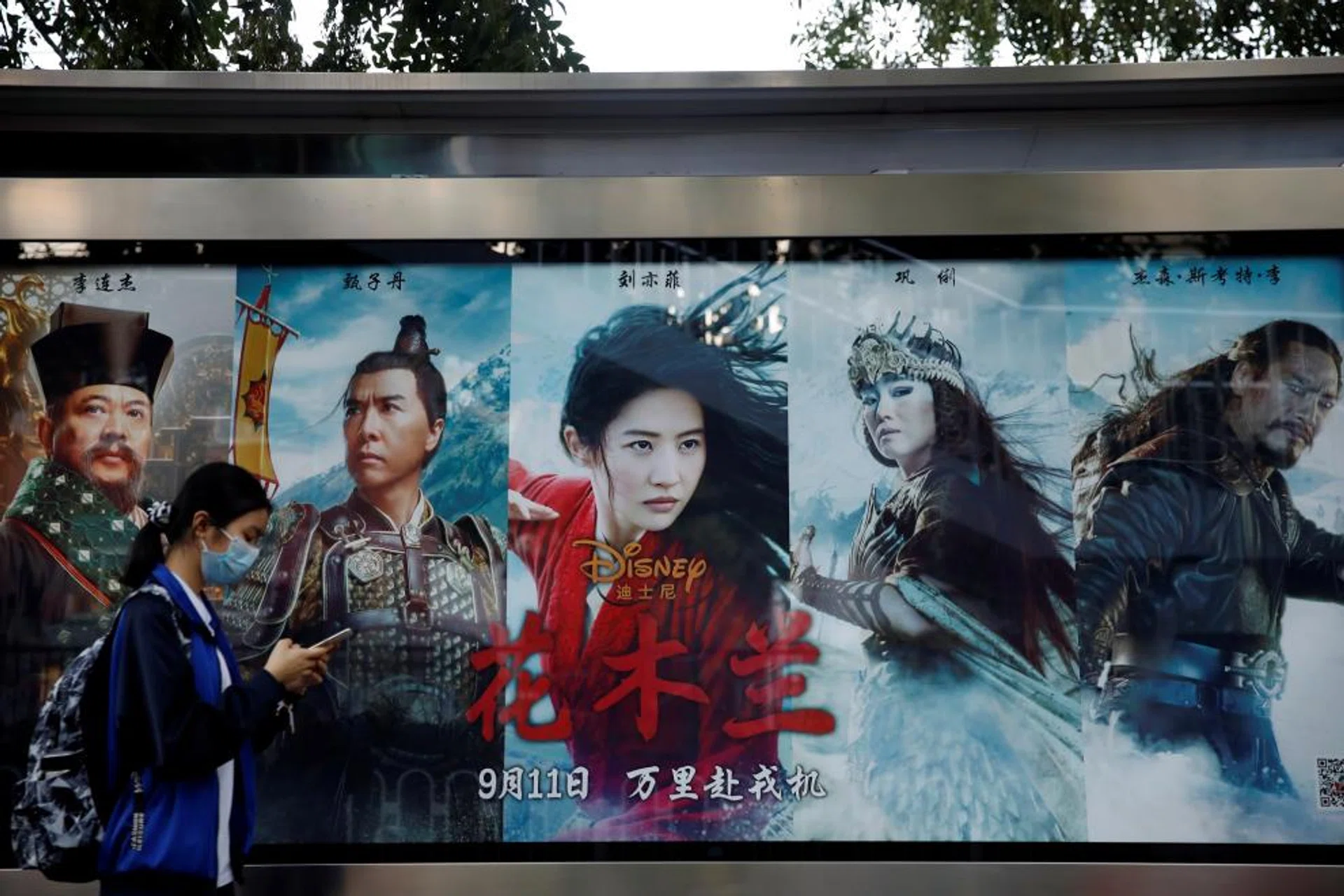 A woman walks past an advertisement promoting Disney's movie "Mulan" at a bus stop in Beijing, China September 9, 2020.