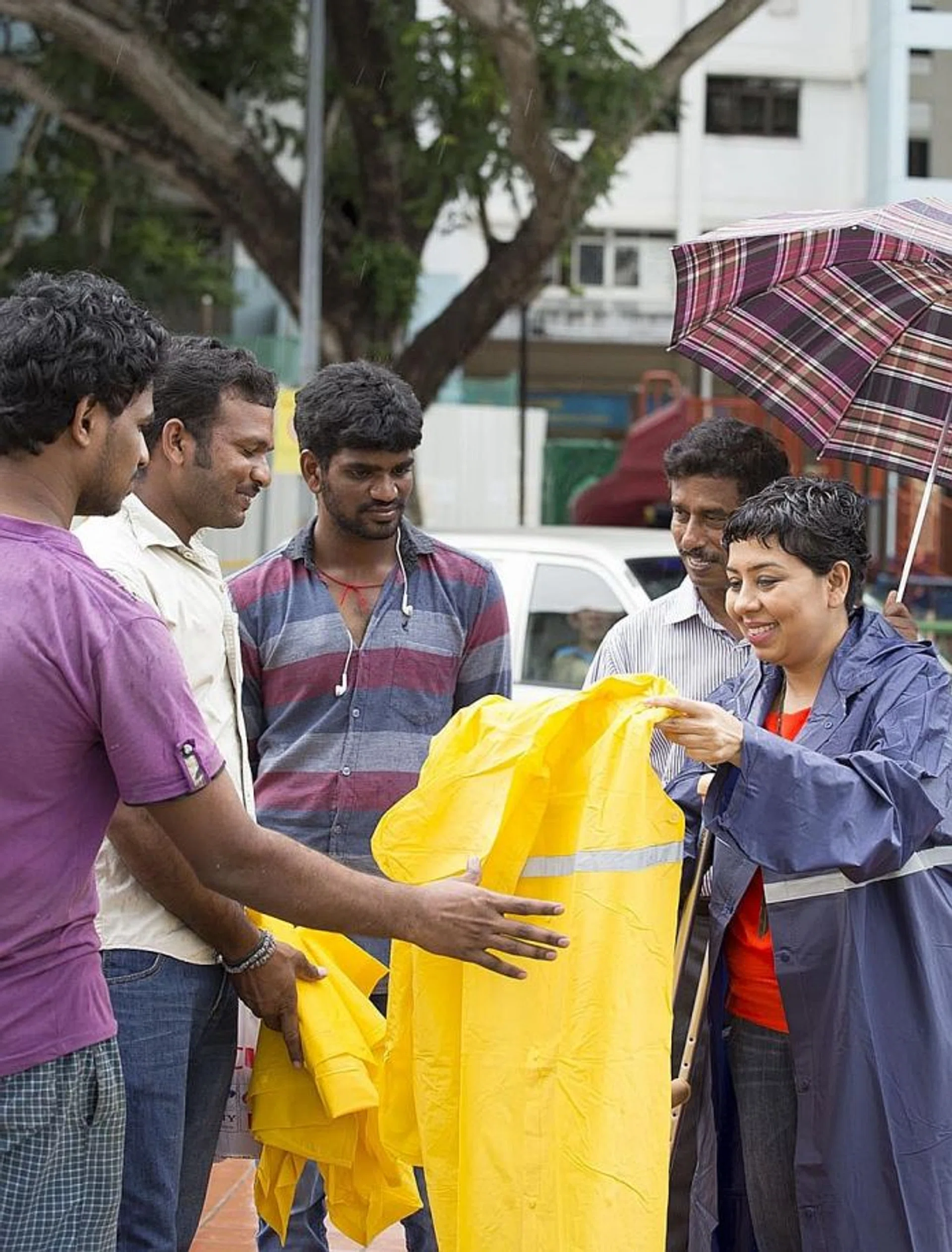 SELFLESS: Ms Dipa Swaminathan (right) distributing raincoats and phone cards to migrant workers at Little India while on crutches.