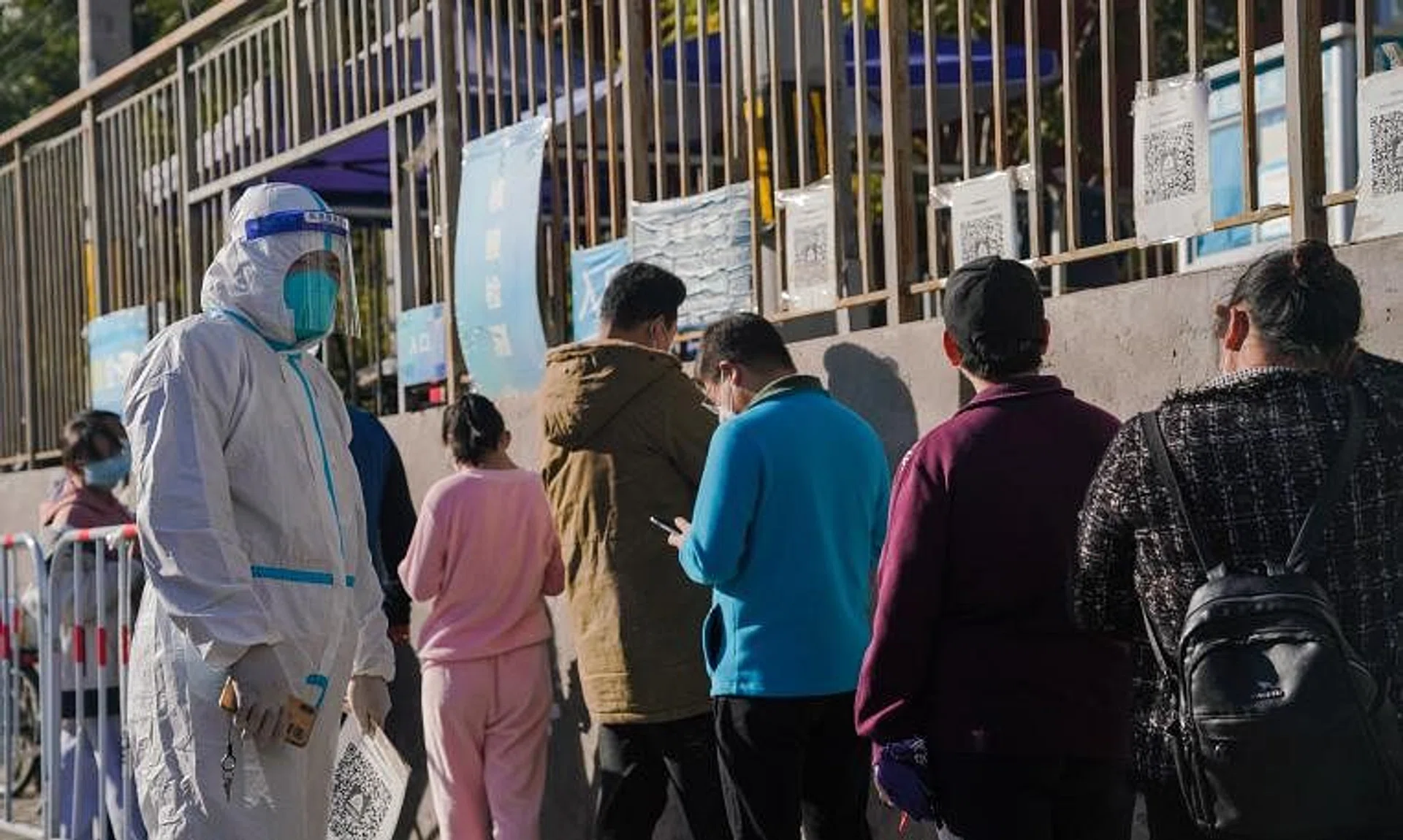 A medical worker wearing a protective suit stands next to a queue of people at a nucleic acid detection point in Beijing.