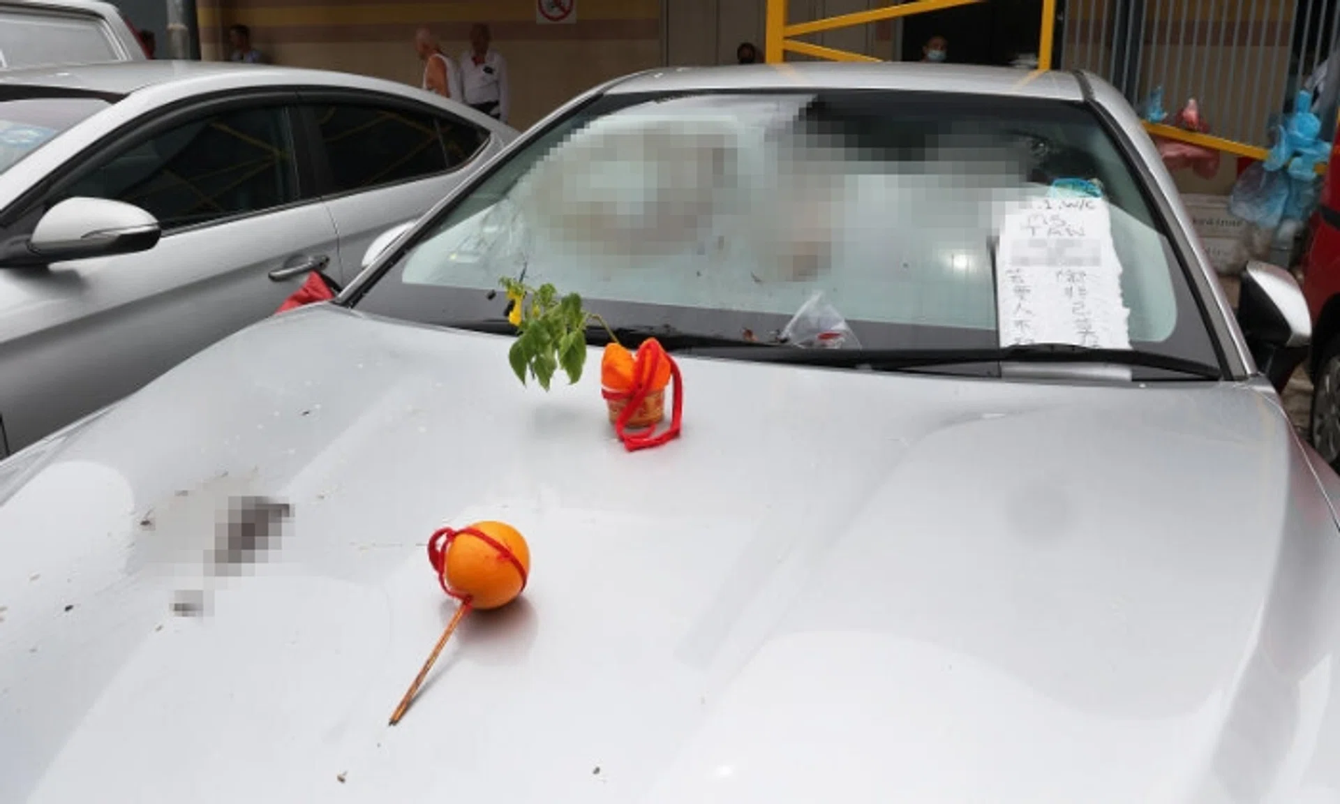 A cake with a flower stuck in it as well as an orange with a red string and two joss sticks were also on the car's bonnet.