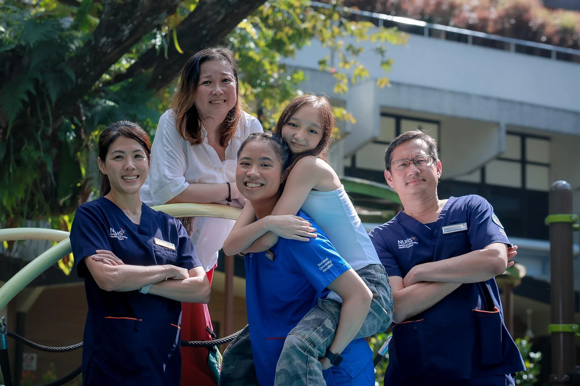Sara Grace Kueh, 17, (piggybacked by older sister, Isabelle Joy Kueh, 26, a staff nurse at NUH) with (from left) Dr Frances Yeap, her oncologist; Mrs Esther Kueh, 52, her mother; and Adjunct Professor Mark Puhaindranon, her surgeon. 