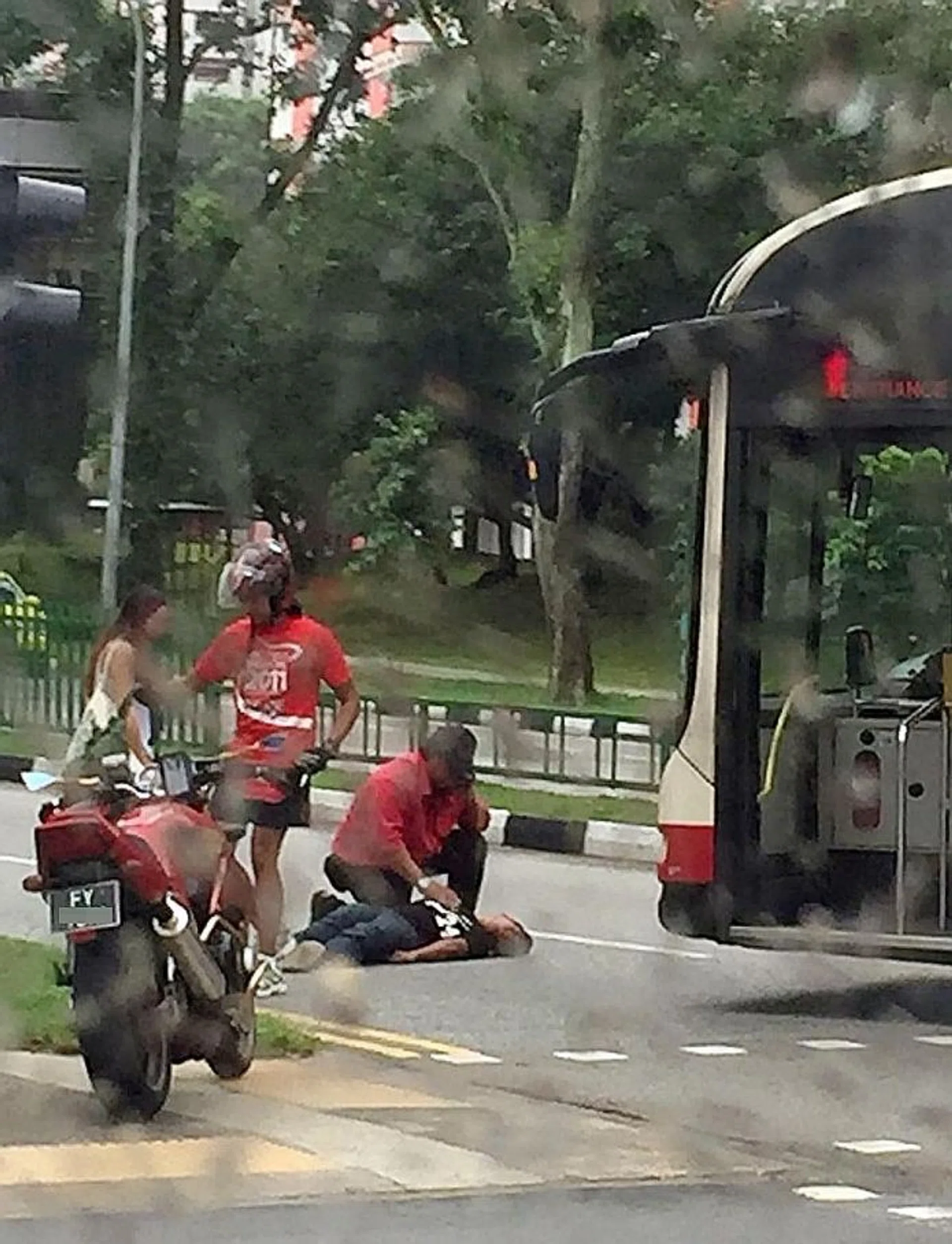 HELP: A bus driver crouching over the boy. A couple on a motorcycle stopped to assist the boy.