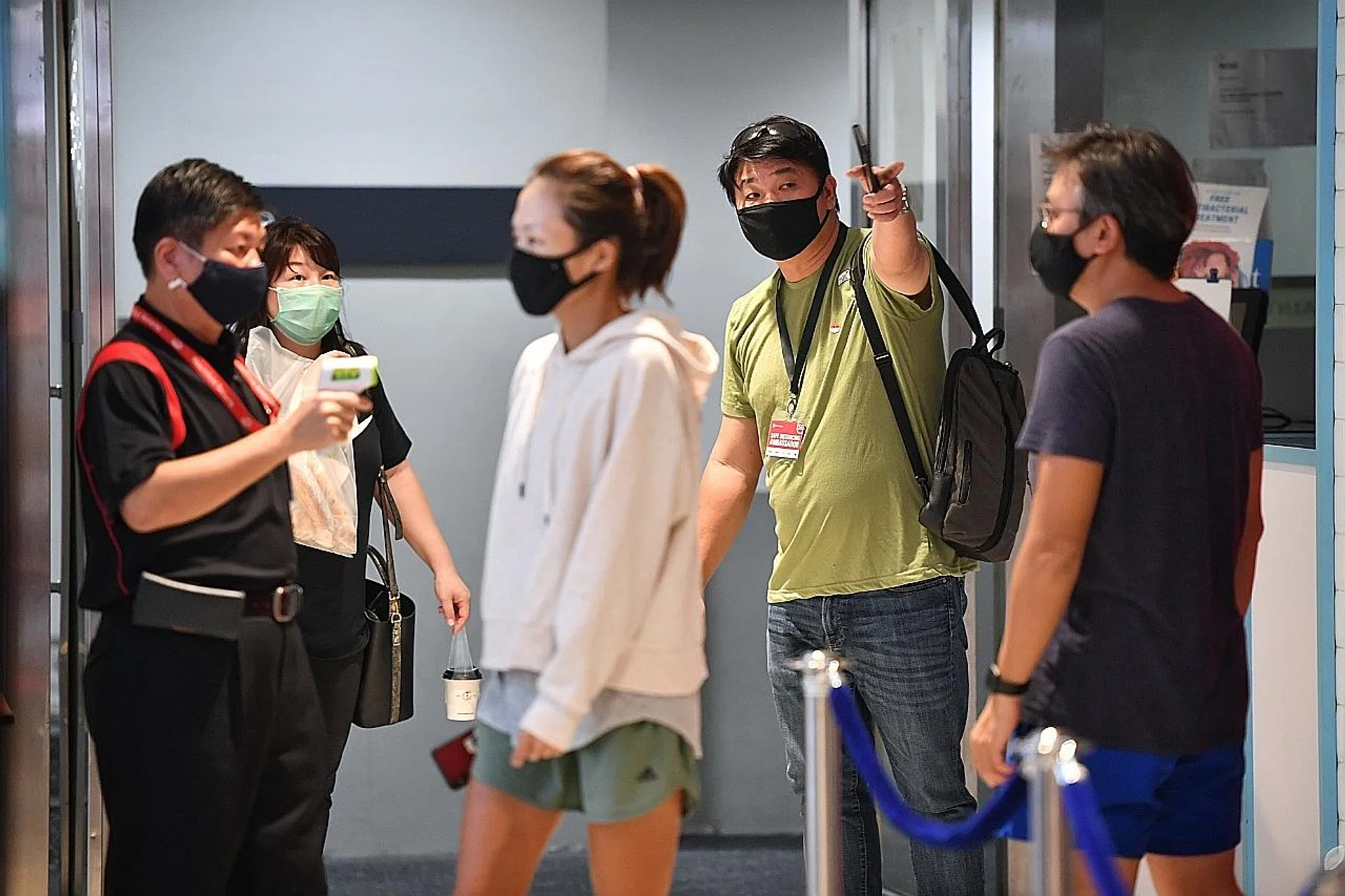 A Safe Distancing Ambassador (in green shirt) guiding people in the queue to enter Clementi Mall. 