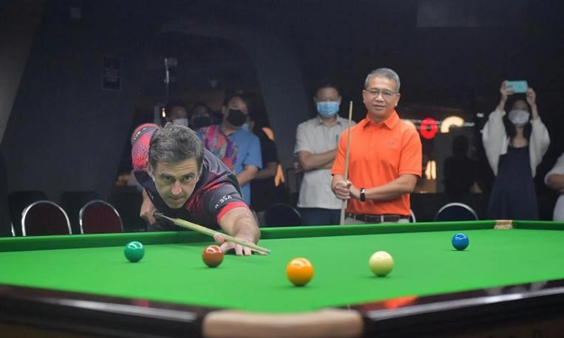 Snooker legend Ronnie O'Sullivan plays a friendly game with Minister Edwin Tong (in orange) at the launch of the Ronnie O'Sullivan Snooker Academy at The Grandstand on June 11, 2022.