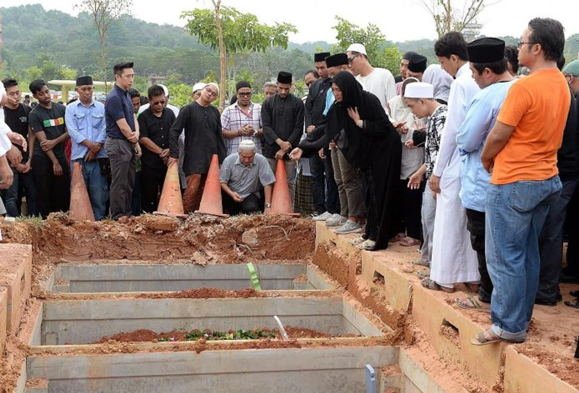 FAREWELL: Mr Asyraf's mother (in black) and Mr Nasrulhudin's father (sitting on the ground) at the burial. Mr Asyraf's mother was seen scattering flowers on both her son's and Mr Nasrulhudin's graves.