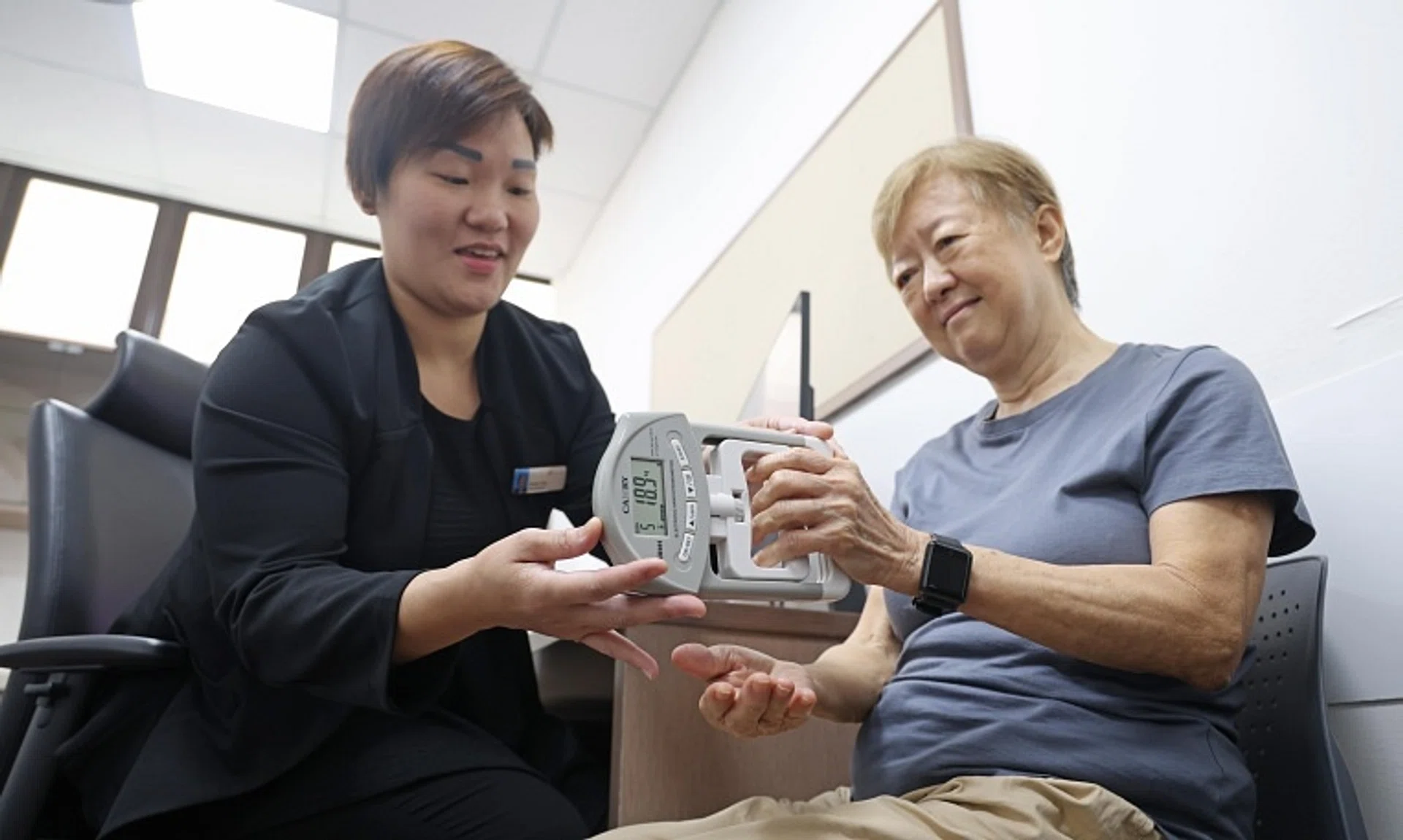 Retired secretary Doris Yam doing a hand grip test under the supervision of Ms Doreen Chan, a senior care coordinator at NHG polyclinics.