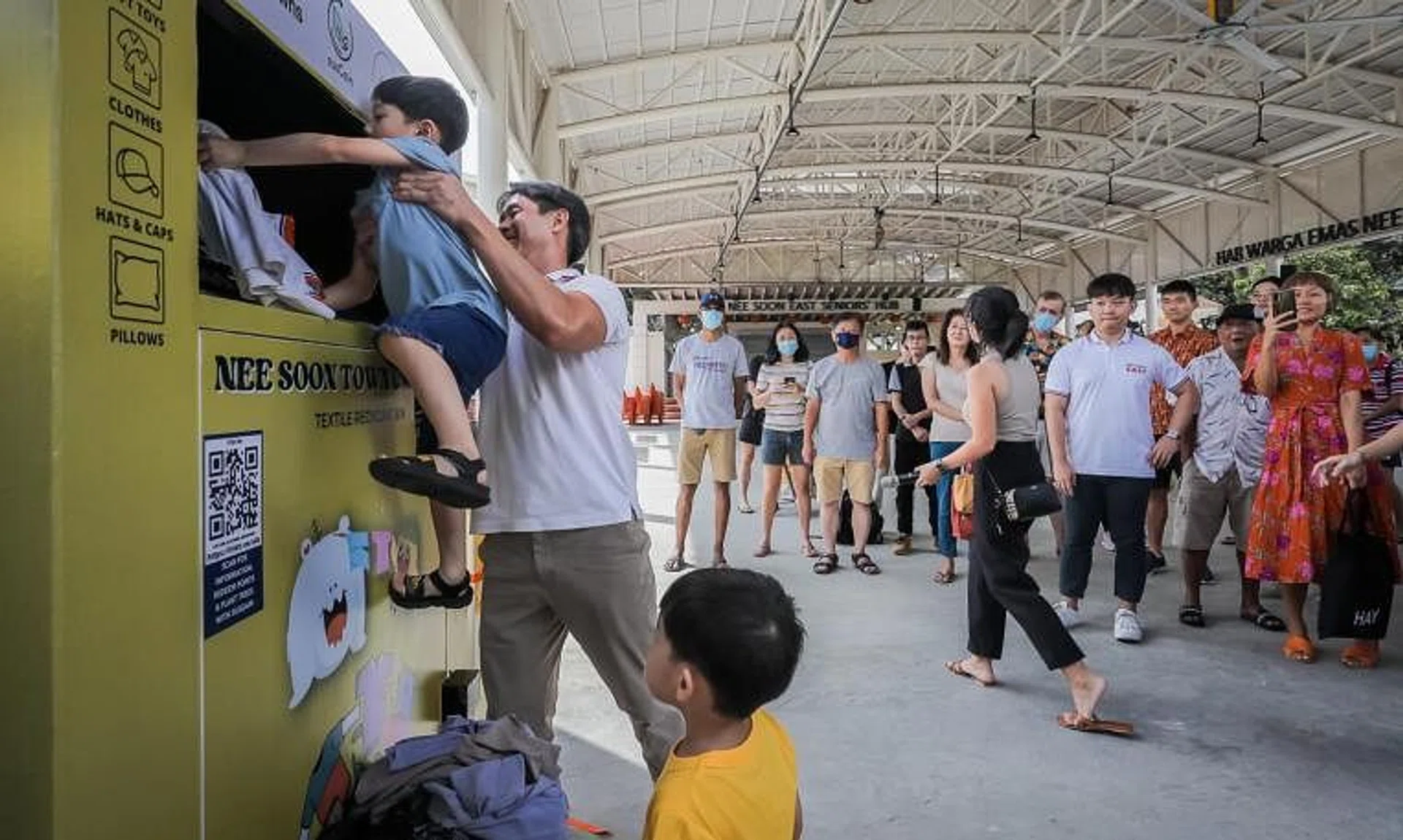 MP Louis Ng helps a young resident put clothes into the textile recycling bin at the launch of Nee Soon Town Council’s recycling hub.