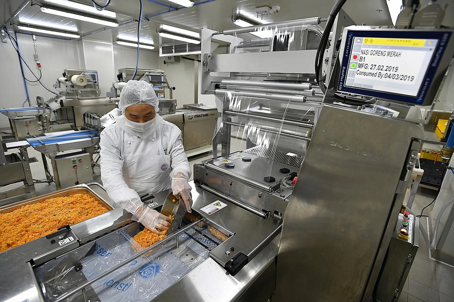 Sats kitchen crew dishing Nasi Goreng Merah into the thermoforming line to extend the product's shelf-life.