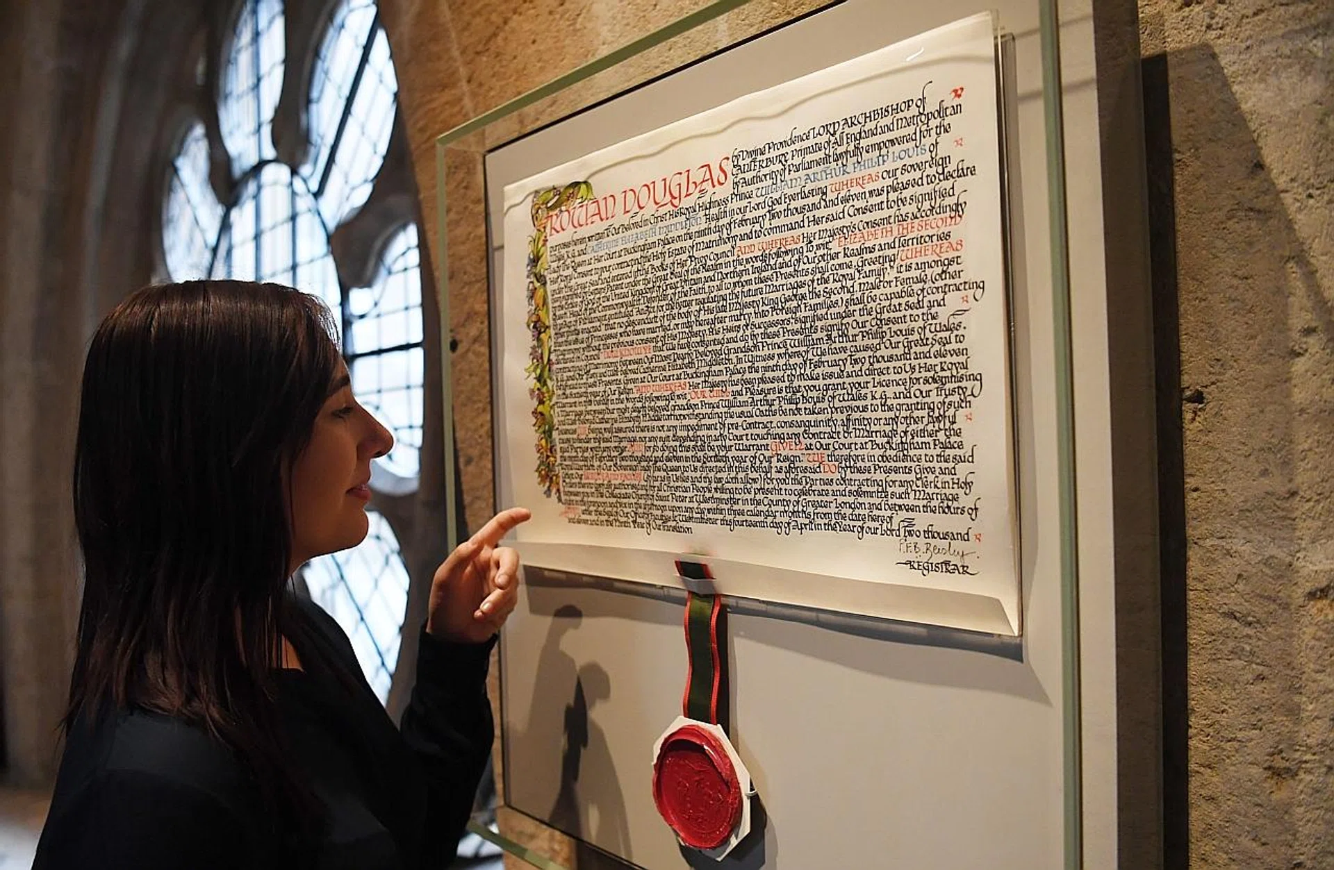 A gallery assistant posing with the marriage certificate of Britain's Prince William and Kate Middleton during a preview of The Queen's Diamond Jubilee Gallery at Westminster Abbey in London. 