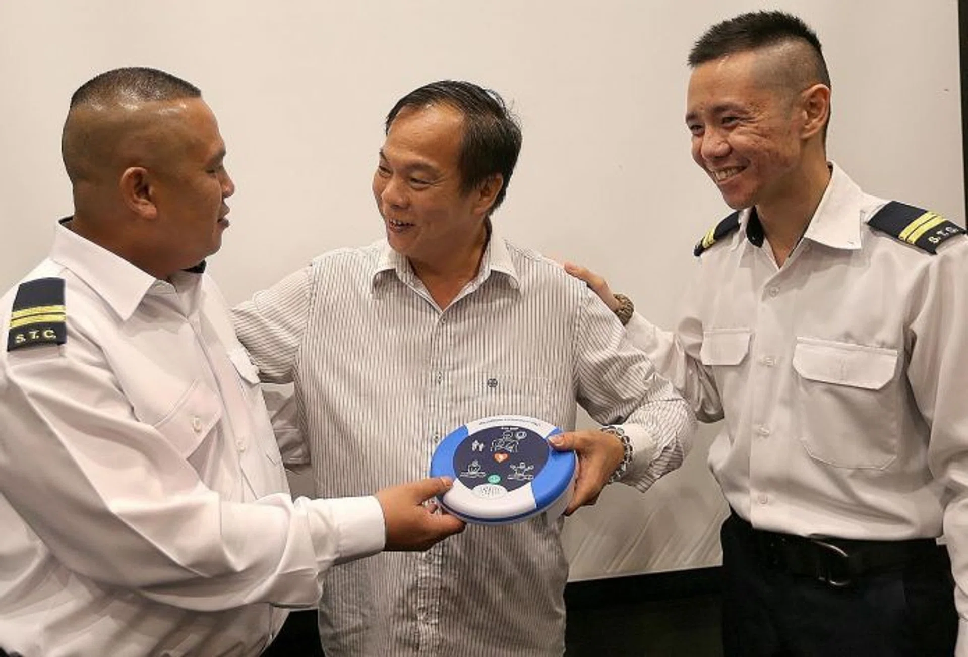 LIFESAVERS: Mr Khoo Teng Guang (middle), holding an AED and thanking senior security officers Mr Hasan Ahmad (far left) and Mr Javerson Chok for saving his life.
