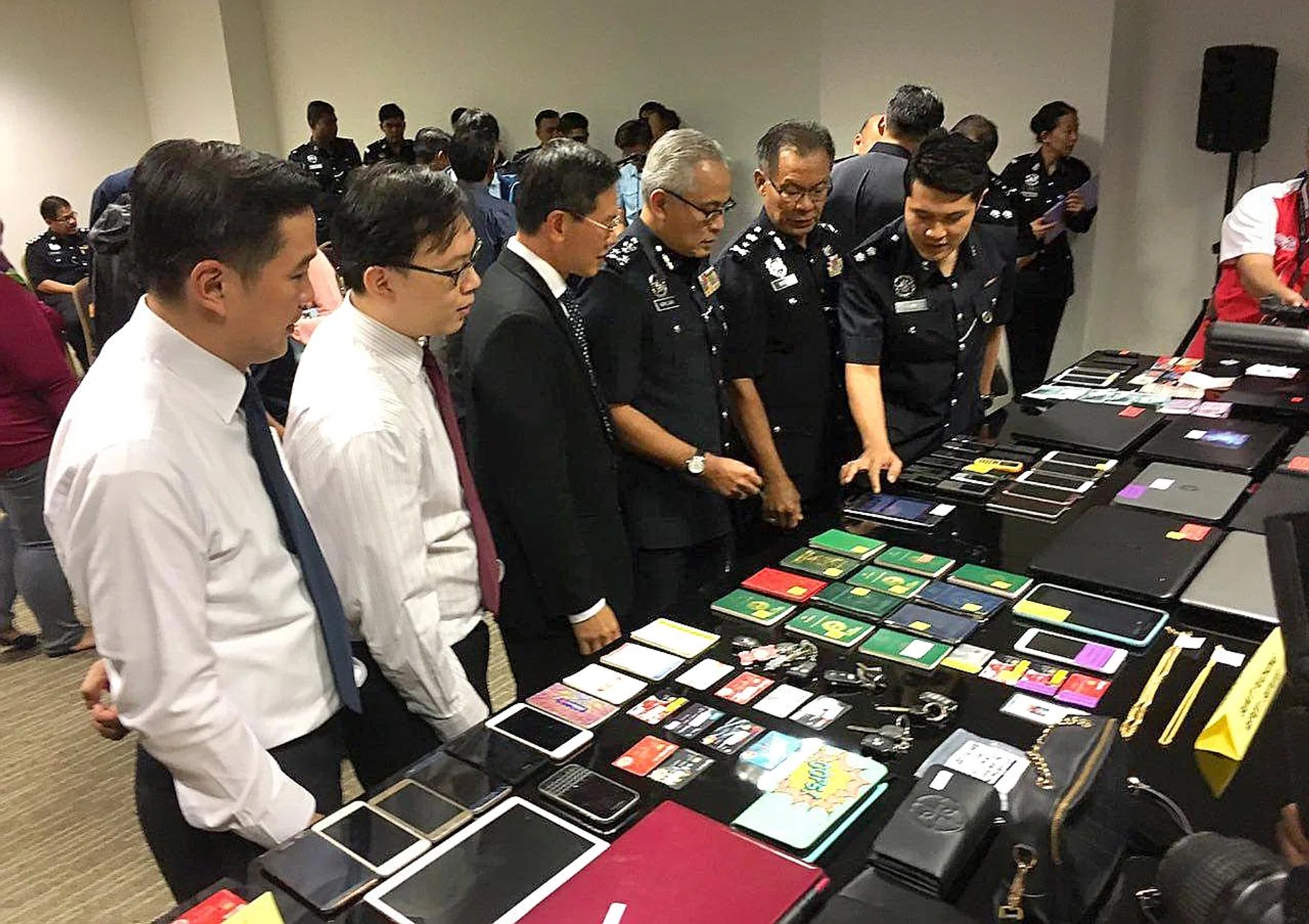 Singapore and Malaysian officers with items seized during the Feb 6-8 joint operation to cripple cross-border Internet love scam syndicates.