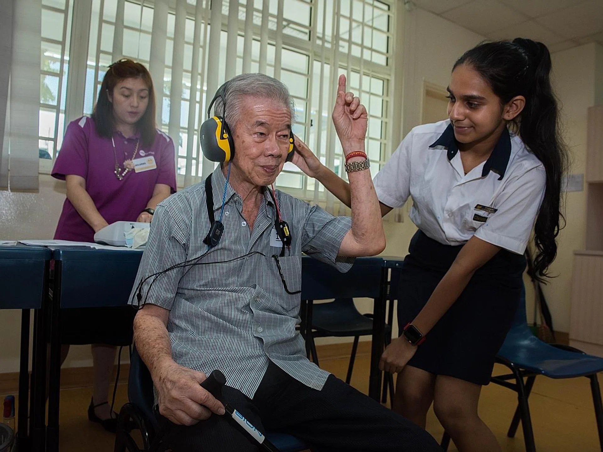 Secondary 2 student Raksha Narayan (right) assisting Mr Koh Tiong San during his hearing screening at Geylang Methodist Secondary School yesterday. TNP PHOTO: SYAMIL SAPARI