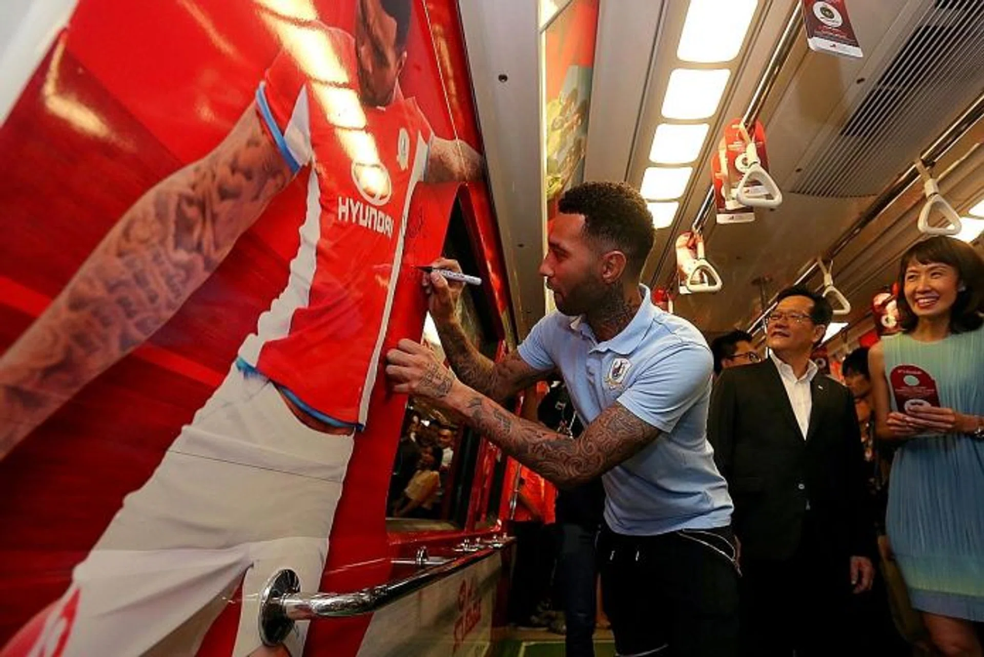 STAR POWER: SMRT's Dawn Low (above) and FAS vice-president Lim Kia Tong watching as Jermaine Pennant signs his name on his poster emblazoned inside a train carriage.  