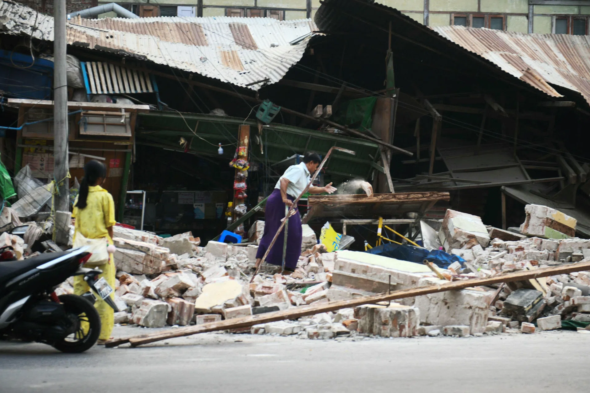 A woman clears debris in front of damaged houses in Mandalay on March 30.