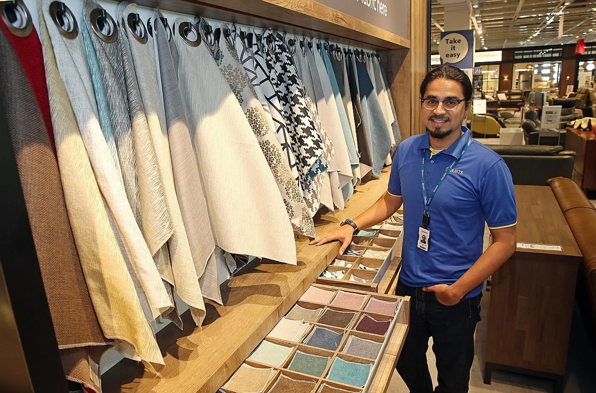 Courts Singapore’s visual merchandising manager Muhammad Rizal showing fabric options for Courts’ made-to-order sofas.