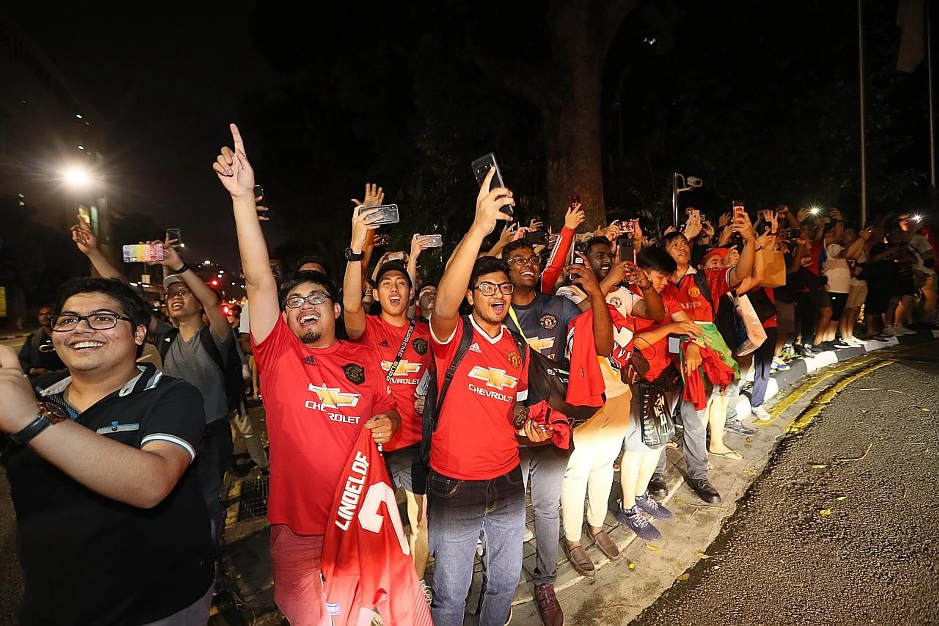 Above: A group of fans, barred from the lobby, standing along Raffles Avenue and waving at the Manchester United bus.