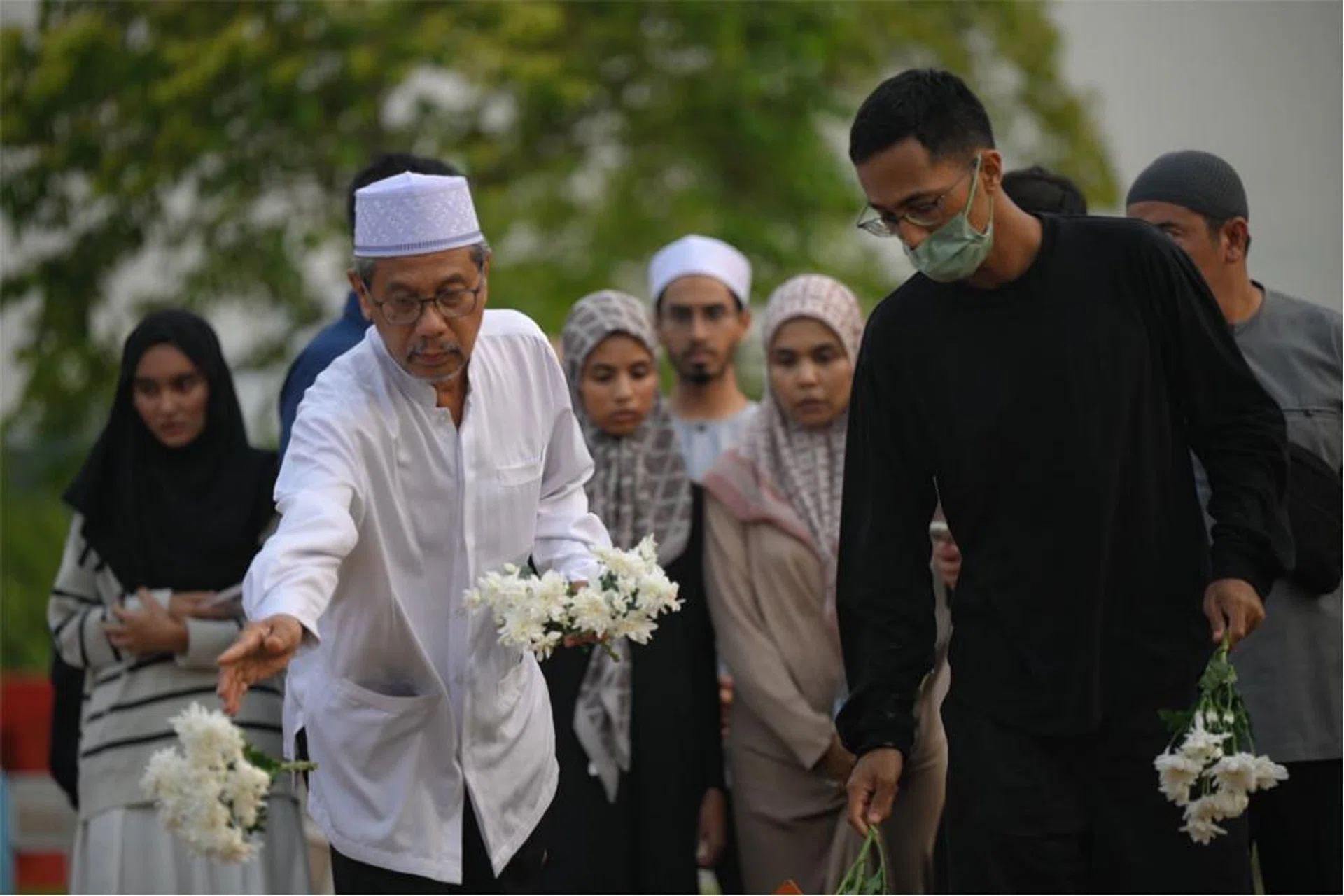Mr Mohamed Kassim Yusoff (in white) placing flowers on his granddaughter's grave.