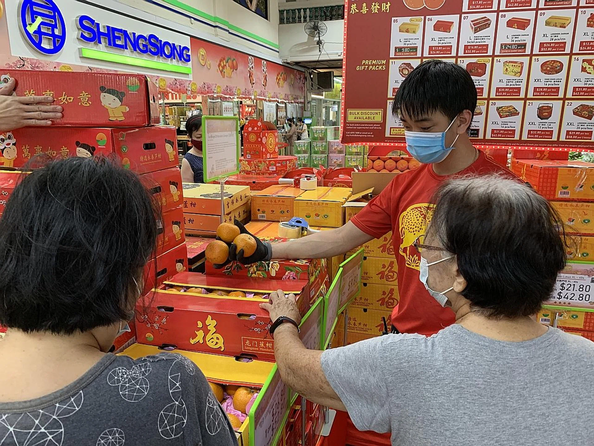 A Sheng Siong employee helps customers check the quality of mandarin oranges for Chinese New Year. The supermarket chain's staff received bonuses of up to 15.72 months last year after it "performed extremely well as compared with previous years". PHOTO