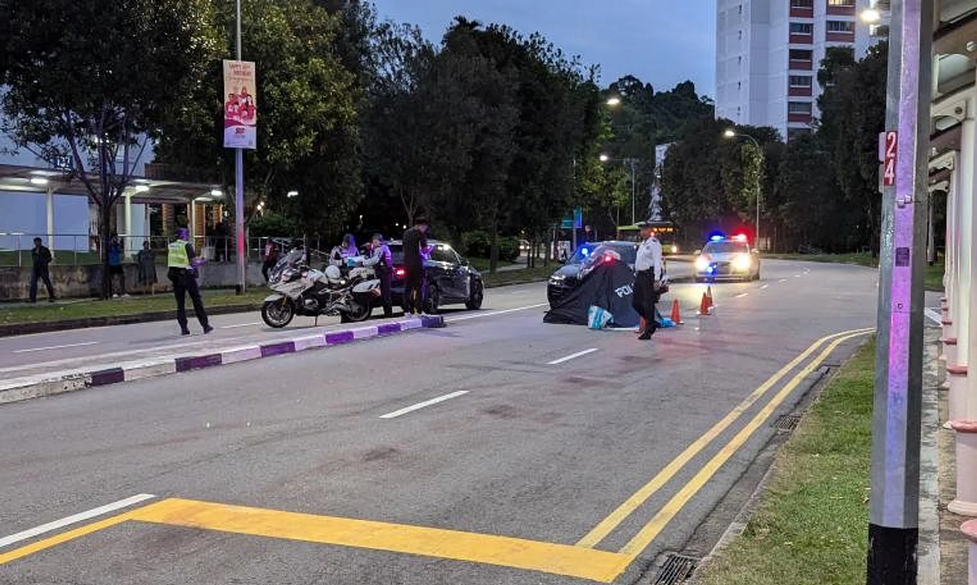 A blue police tent is erected on the right lane of a two-lane dual carriageway, next to the road divider.
