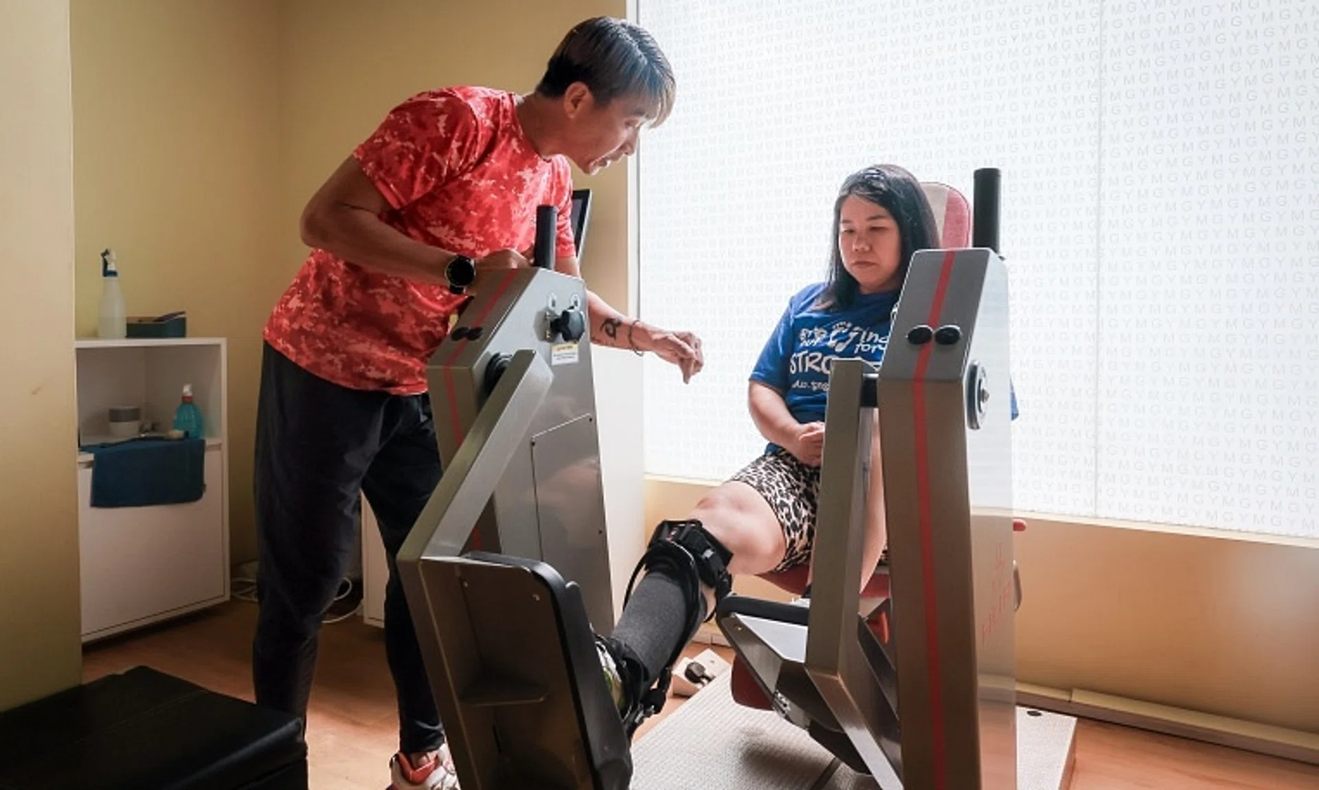 ActiveSG Instructor Victor Ng, 51, helps stroke survivor Maya Seah, 44, as she works on strengthening her legs at the Enabling Village ActiveSG Gym on Dec 19.