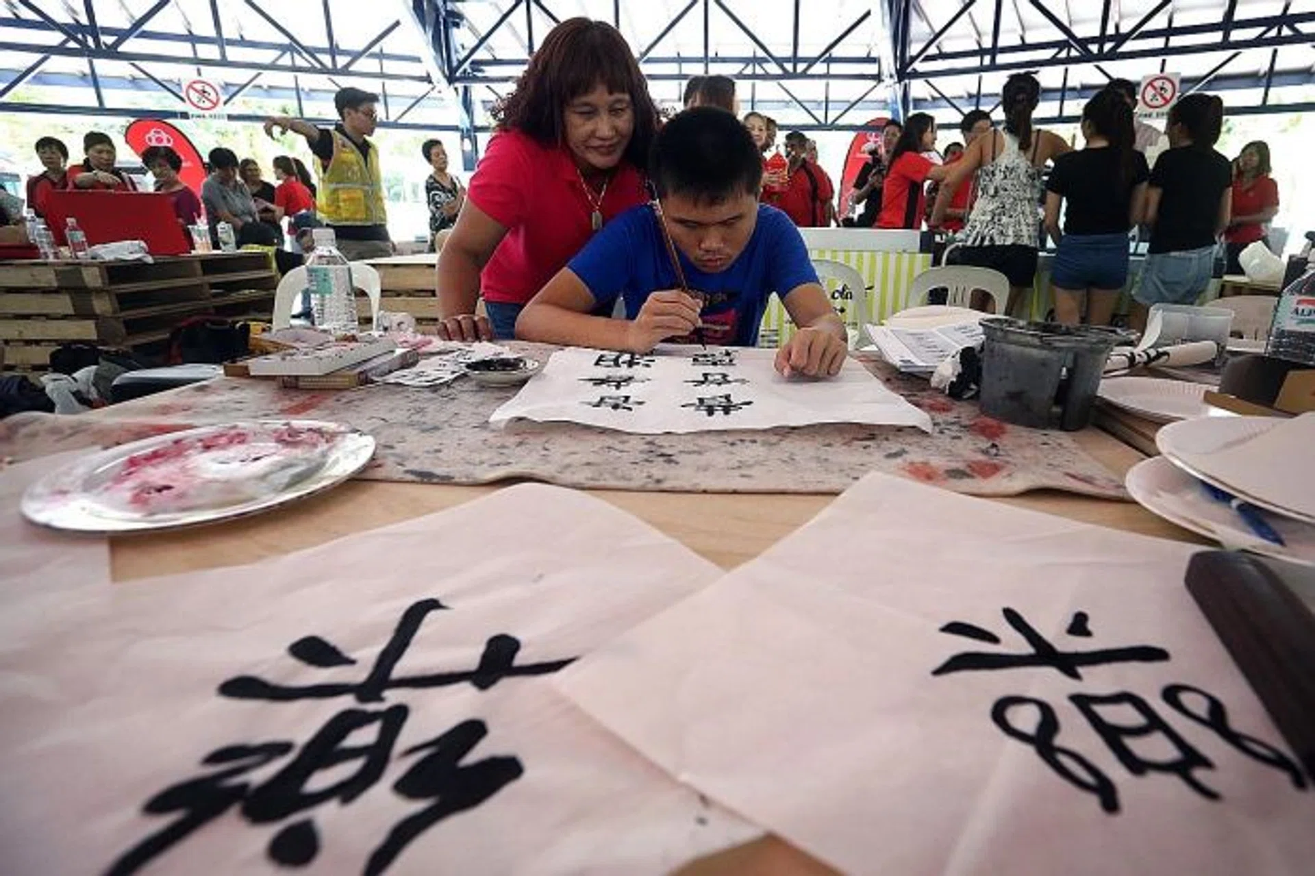 FOCUSED: (Above) Leow Wei En, 18, was introduced to calligraphy just seven months ago. At the Rock Our Blocks party, he demonstrated his skill with confidence. His mother Jocelyn Toh, 52, watches as he practised his craft.
