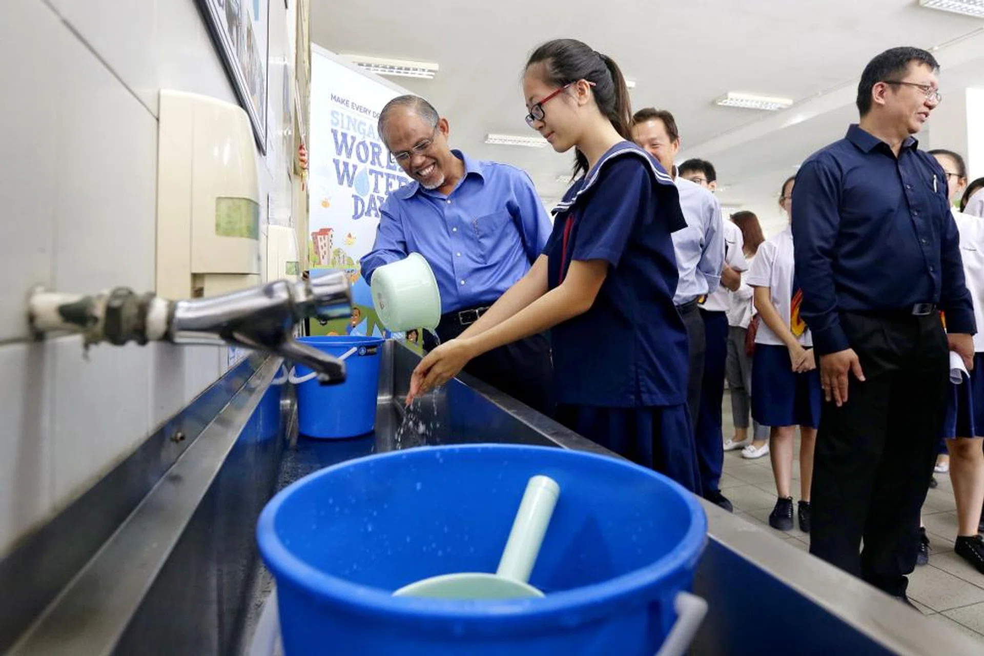 Minister for the Environment and Water Resources Masagos Zulkifli and Secondary Two student Koh Wei Shan rationing the use of water collected in a bucket at Woodgrove Secondary School on Mar 1, 2017.
