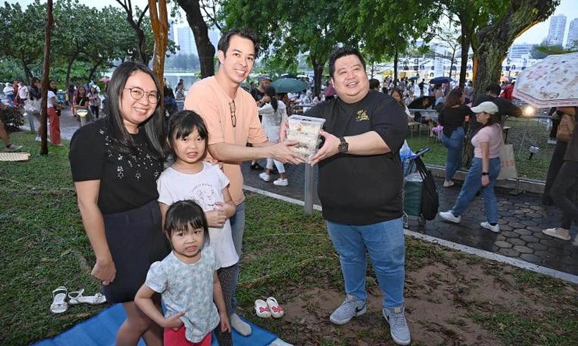 Feng Sheng owner Tong Chun Wee (in black top) giving away chicken rice packs to a family of Swifties at the National Stadium on March 7.
