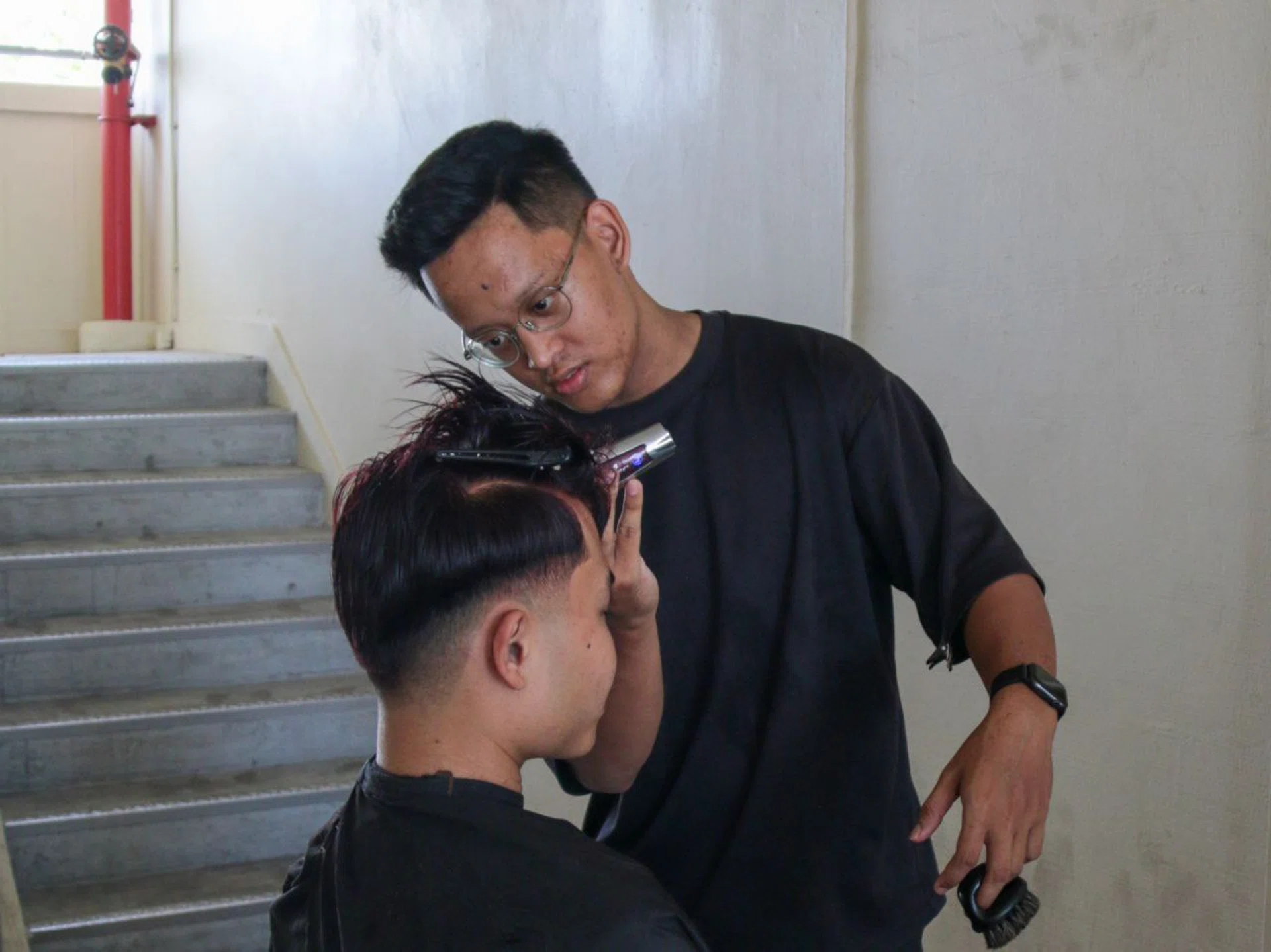 Muhammad Hazim Hanif, 23, cuts his friend's hair in the comfort of the lift lobby of his home.