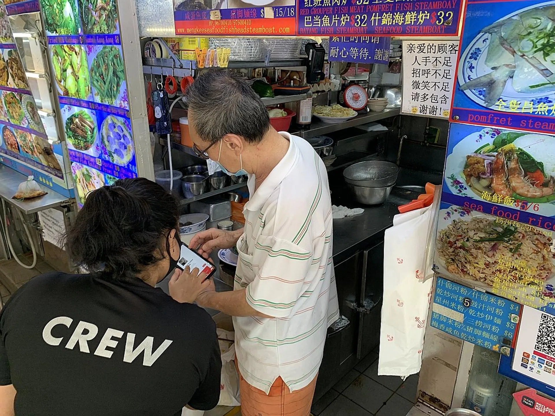 A BySGForSG team member helping Mr Yeo See Hock of Meng Kee Seafood learn how to use the platform's ordering system.