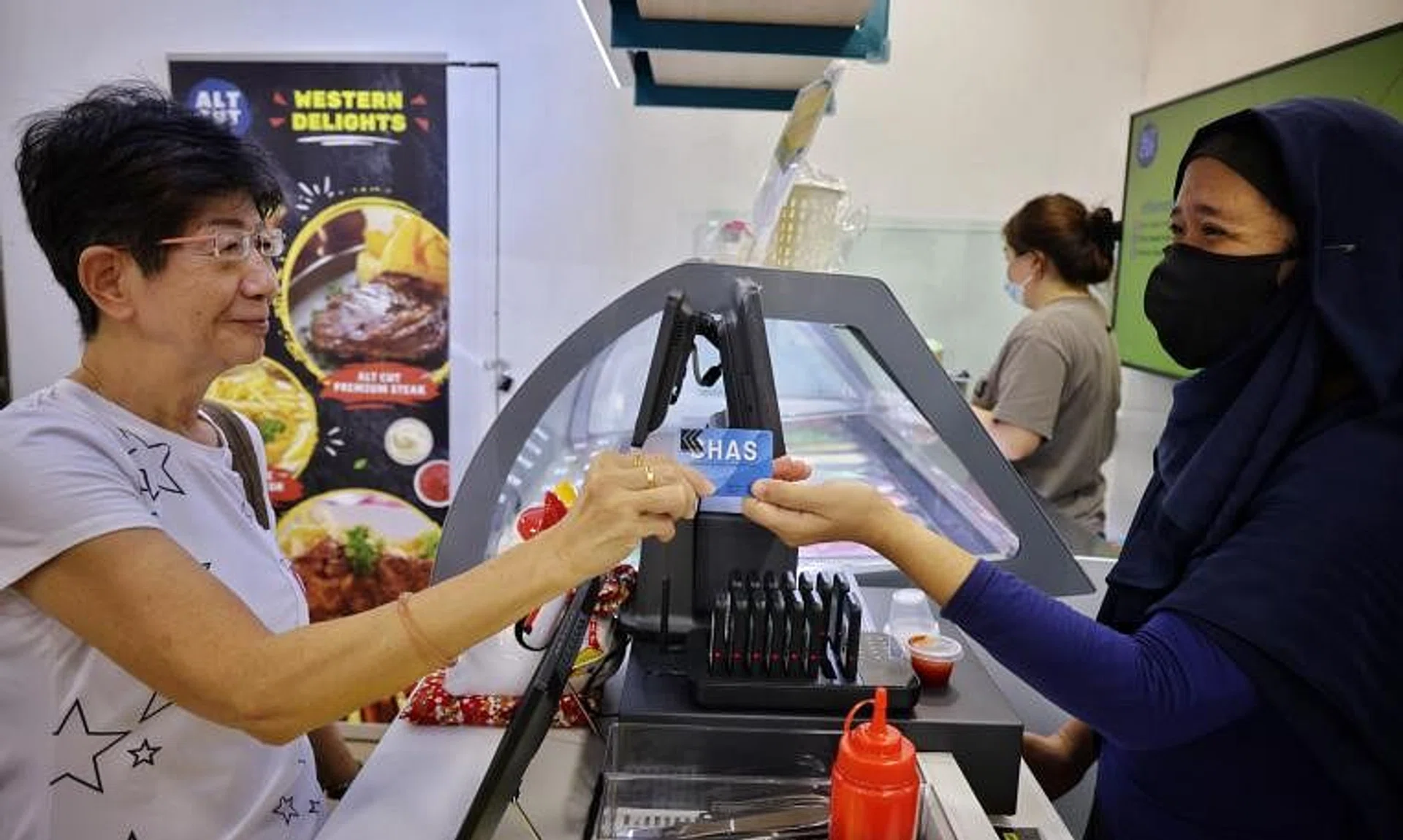 Mdm Rena Tan (left) using her CHAS card with a Kampong Chai Chee sticker, at the launch of the Gd Lobangs @ KCC programme.