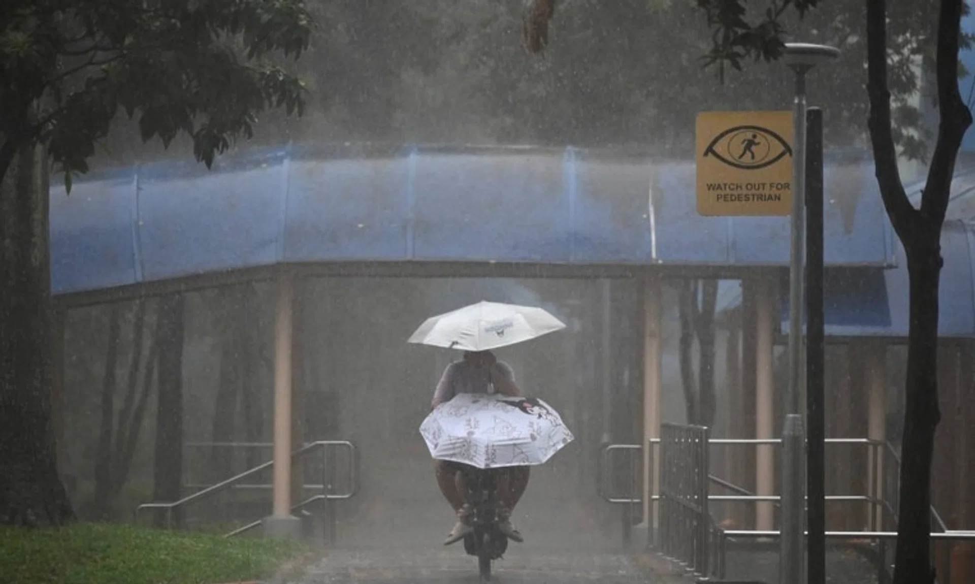 A woman riding an e-scooter with a child while holding an umbrella under the heavy rain next to Block 846 Tampines Street 82 at 8.46am on Oct 14.