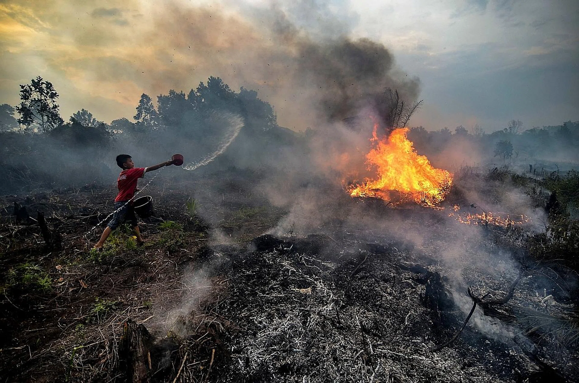 A young boy attempting to extinguish a fire in his neighbourhood in Pekanbaru, Riau province, Indonesia. 