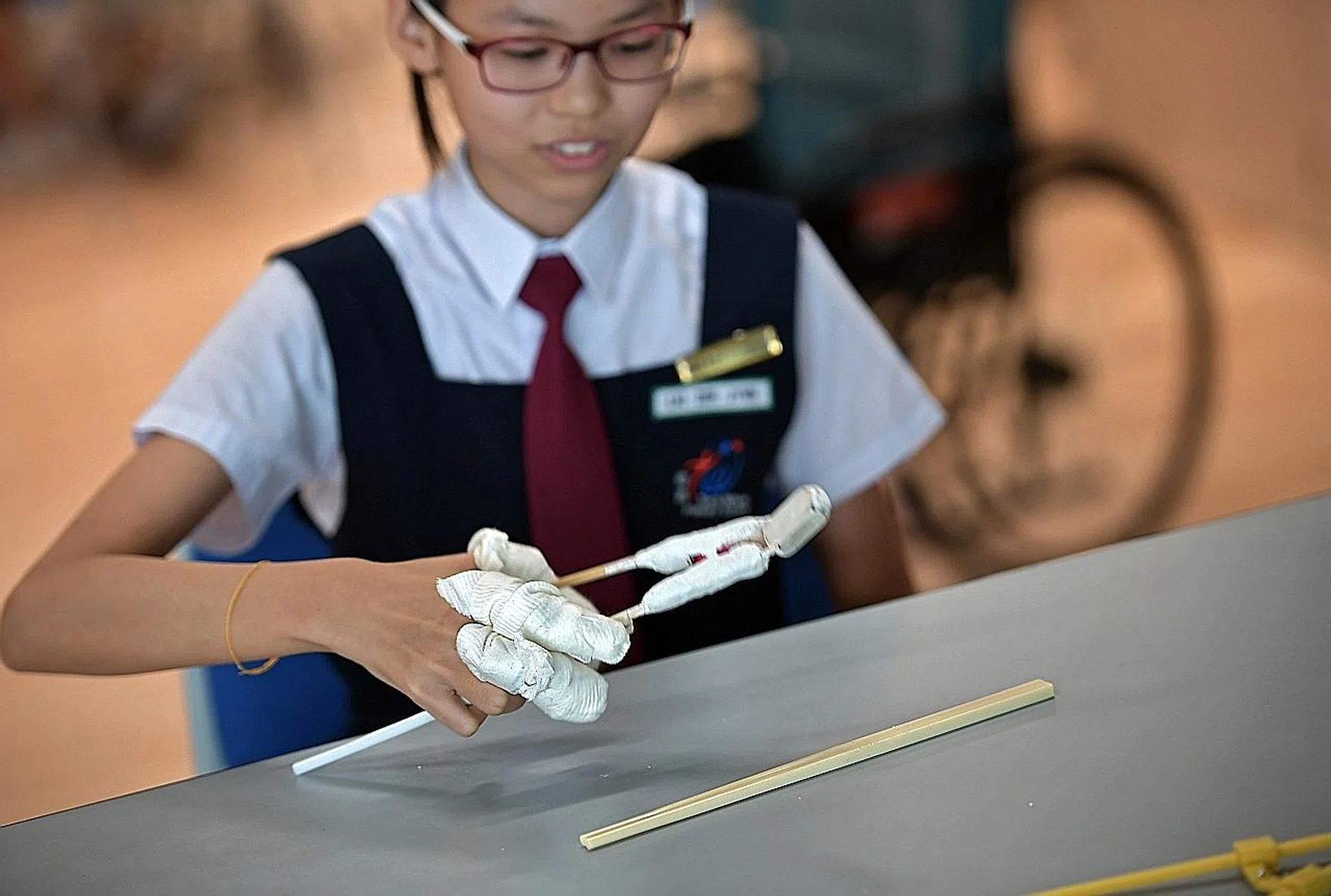 Teck Whye Primary pupil Lai Zer Jynn making use of the spring-operated chopsticks she innovated with her friends. Her fingers are wrapped up to reduce finger dexterity. 