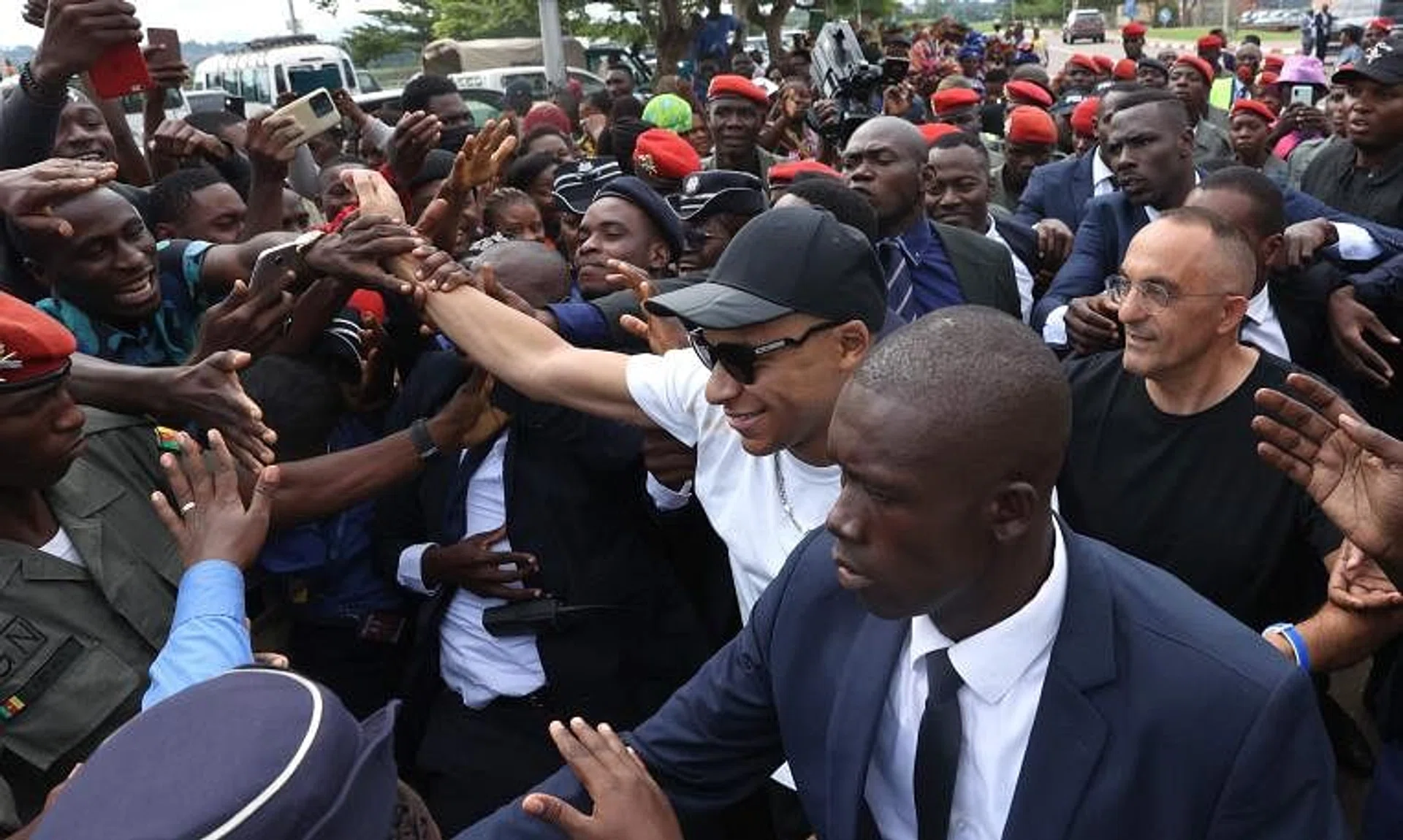 PSG striker Kylian Mbappe (centre) greets crowds gathered outside Yaounde airport.