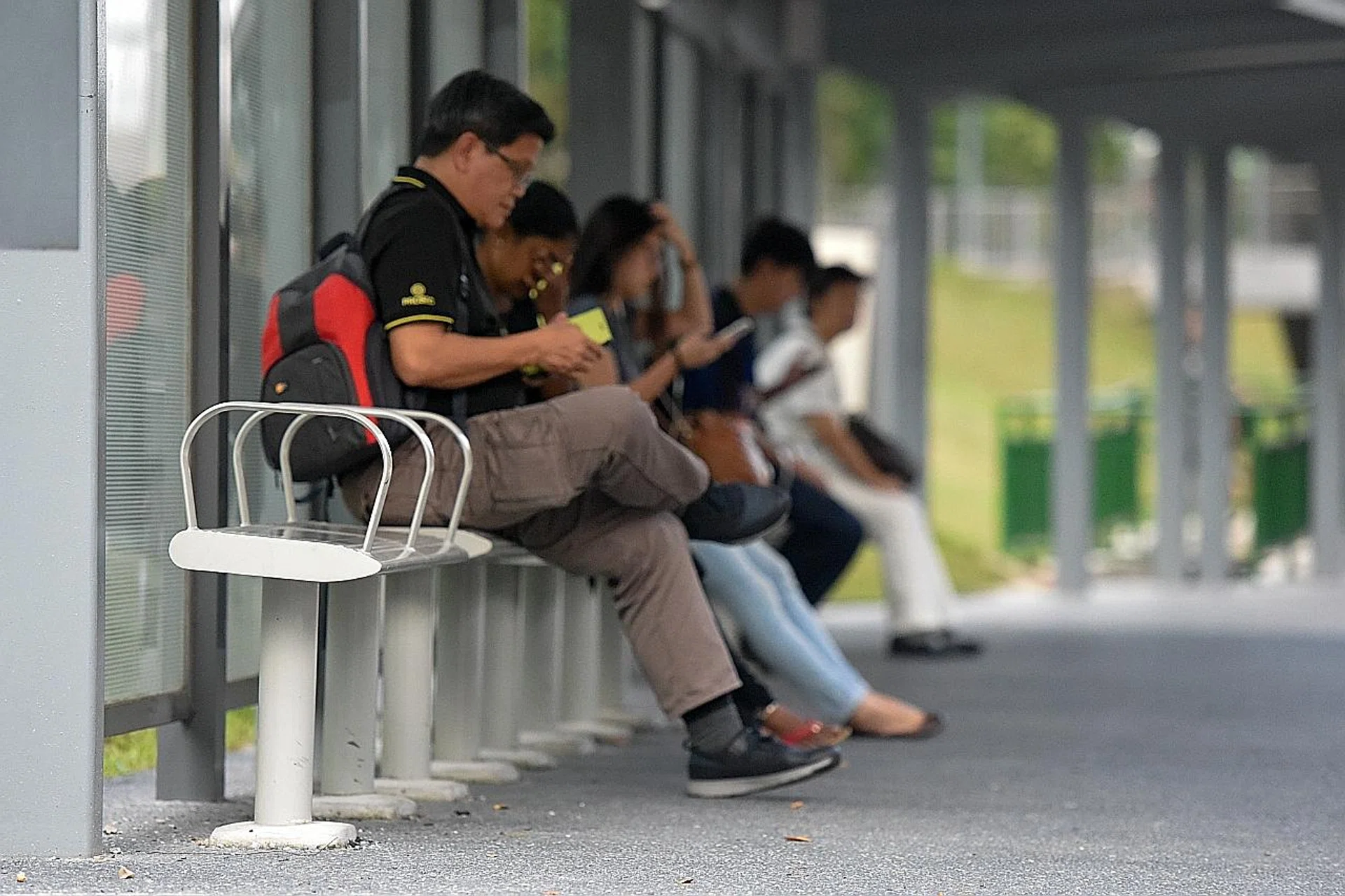 People sitting on the wider benches at a bus stop in Braddell Road.  