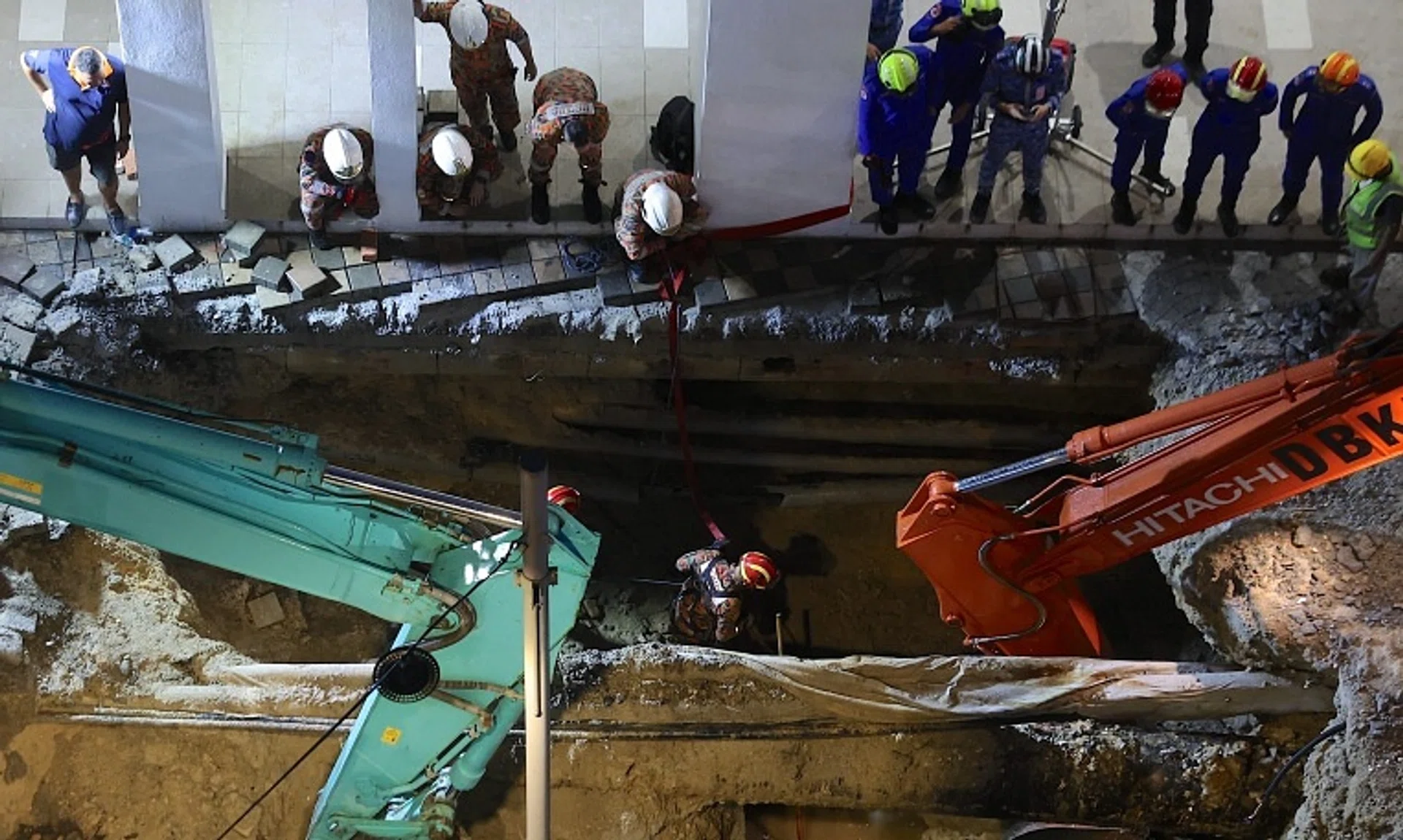 Malaysia Fire and Rescue Department officers inspect the site where a woman fell into an 8m-deep sinkhole in Kuala Lumpur.