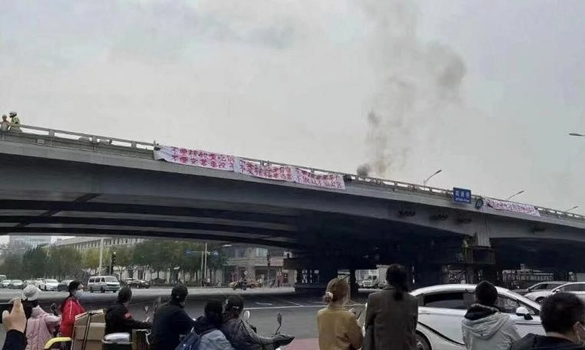 People watch while smoke rises as a banner with a protest message hangs off Sitong Bridge in Beijing on Oct 13. Hundreds of WeChat users have had their accounts blocked after making reference to the demonstration that called for President Xi's ouster. 