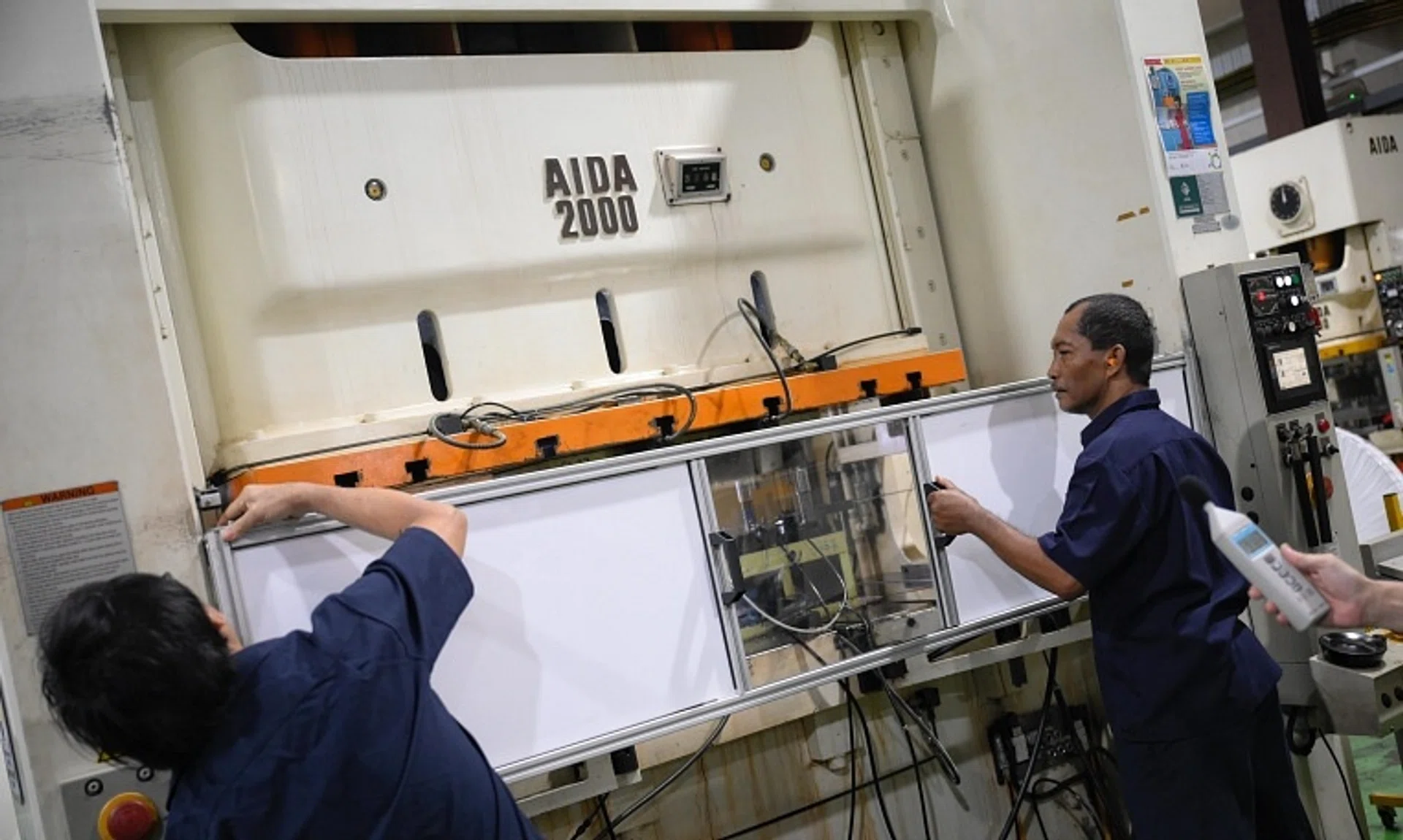 Floor supervisors attaching a sound shield with material which absorbs noise onto a metal stamping machine for bicycle components at Nakano Metal Press on Oct 17.